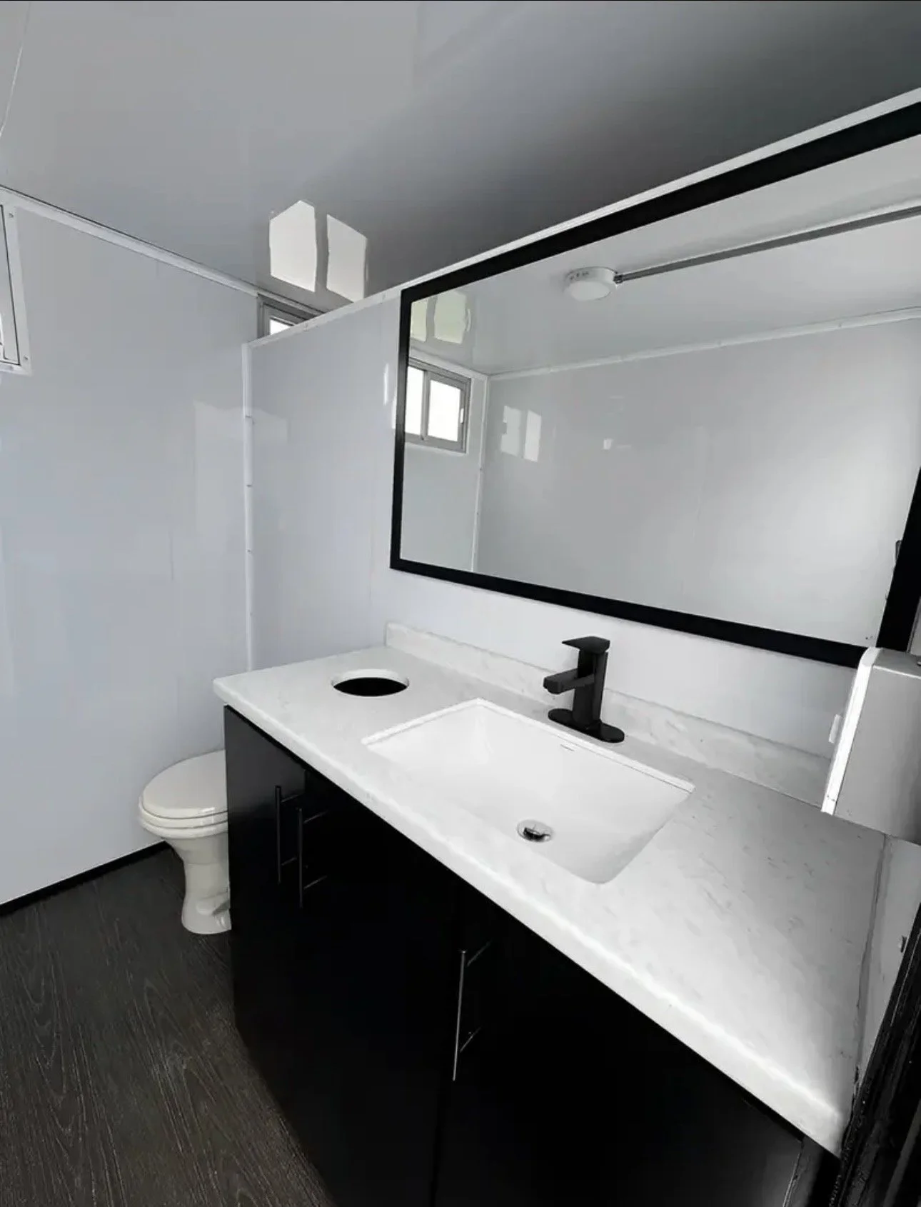 Modern bathroom with black vanity, white marble countertop, large mirror, black faucet, white toilet, small windows, and gray flooring.