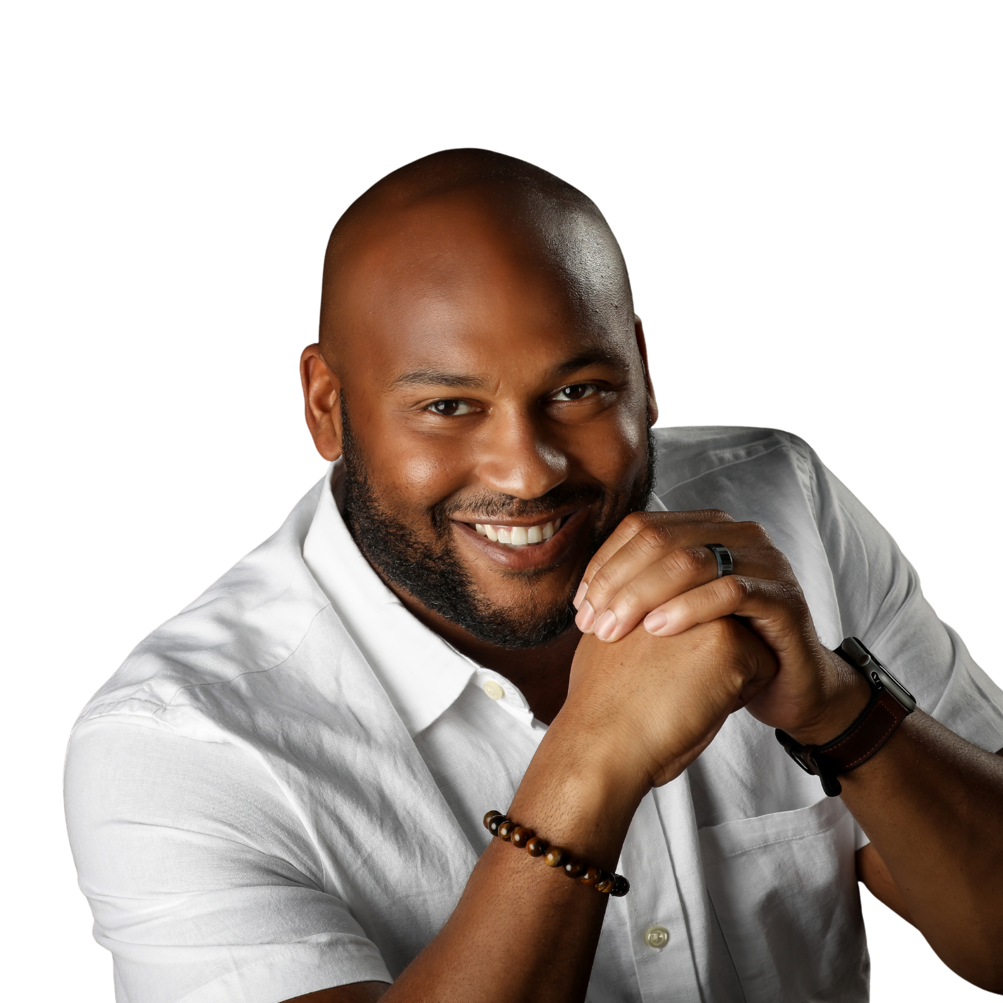 A smiling man with a beard and bald head wearing a white shirt, looking directly at the camera with hands clasped together and wearing a black wristwatch and beaded bracelet.
