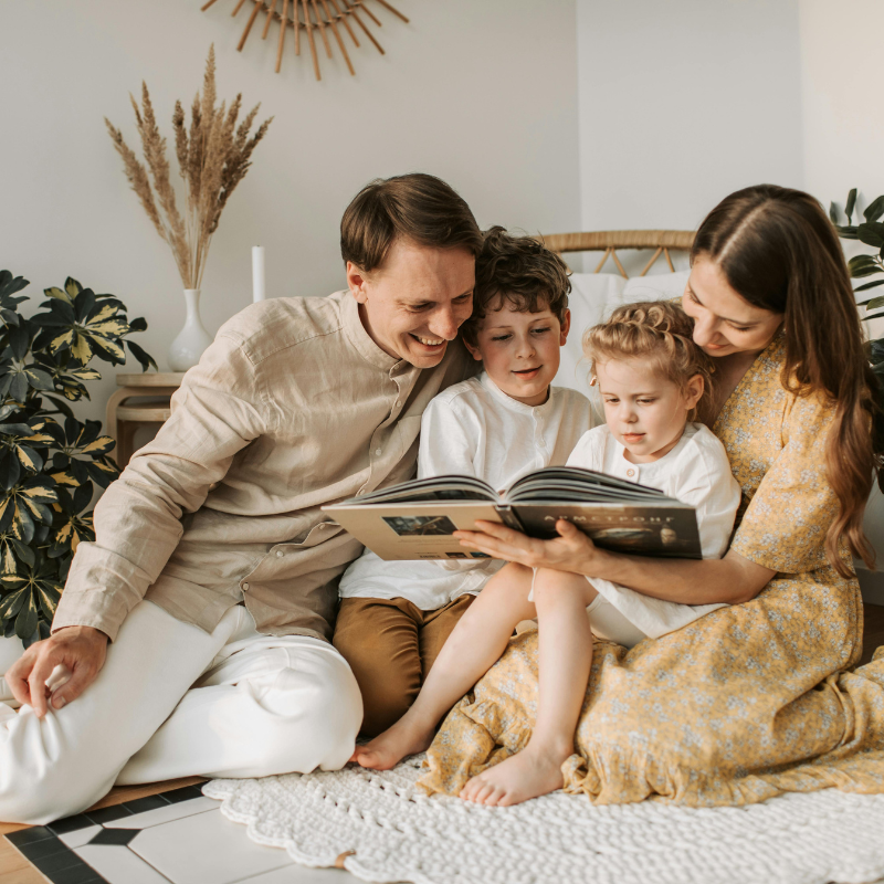A family of four sitting on the floor reading a photo album together in a cozy living room.