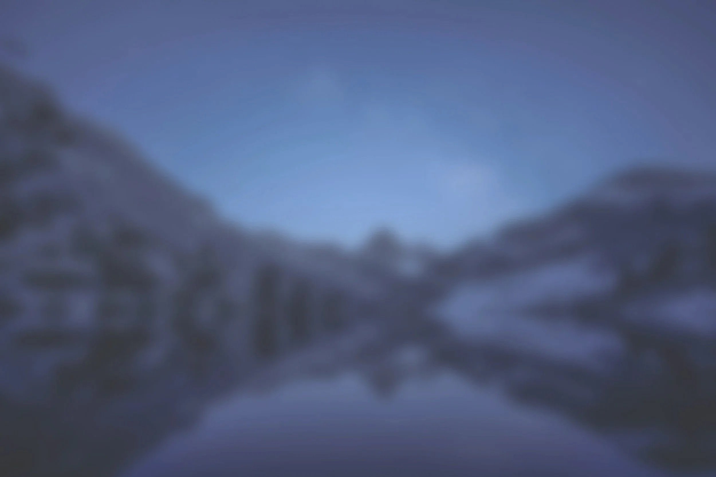 Blurred image of a landscape with snow-covered trees and a clear sky in the background.