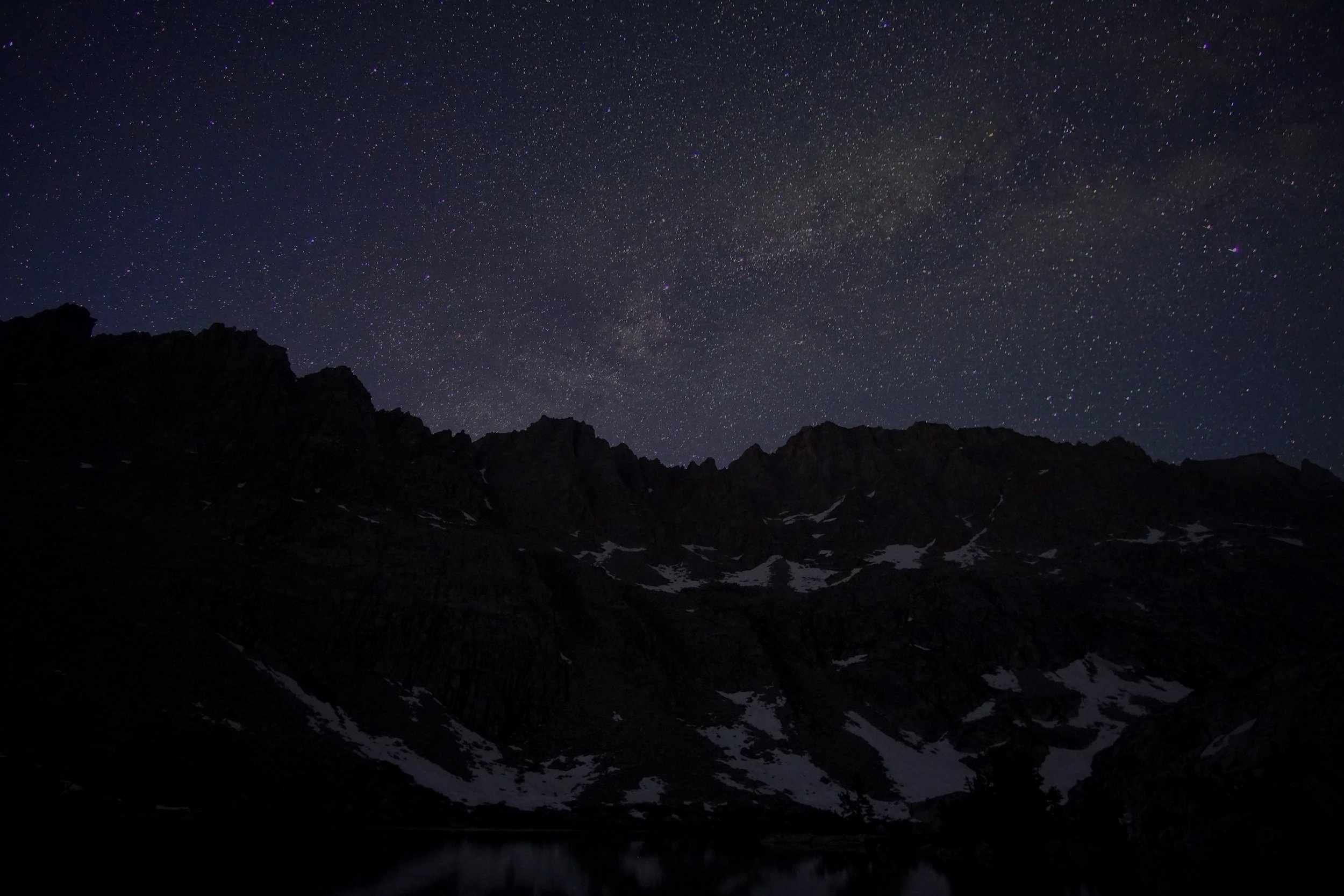 Night sky filled with stars over a silhouetted mountain range with patches of snow.