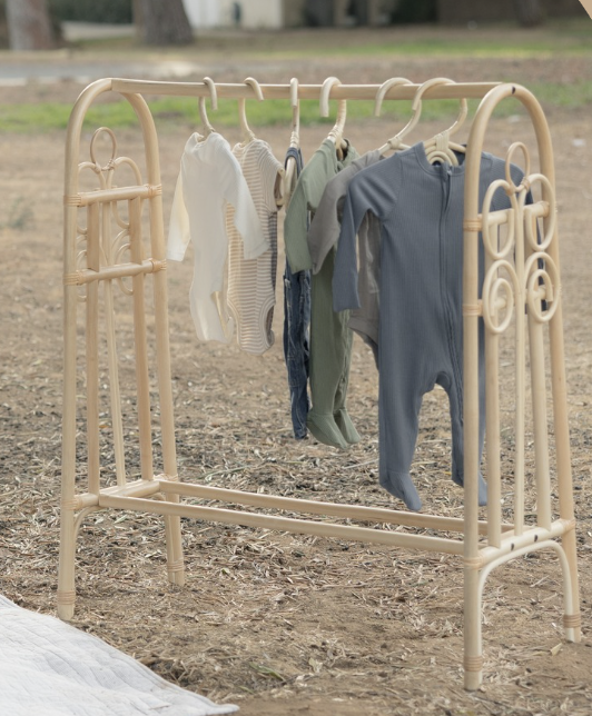 Clothes hanging on a baby clothes rack outdoors, including baby onesies and rompers in various colors.