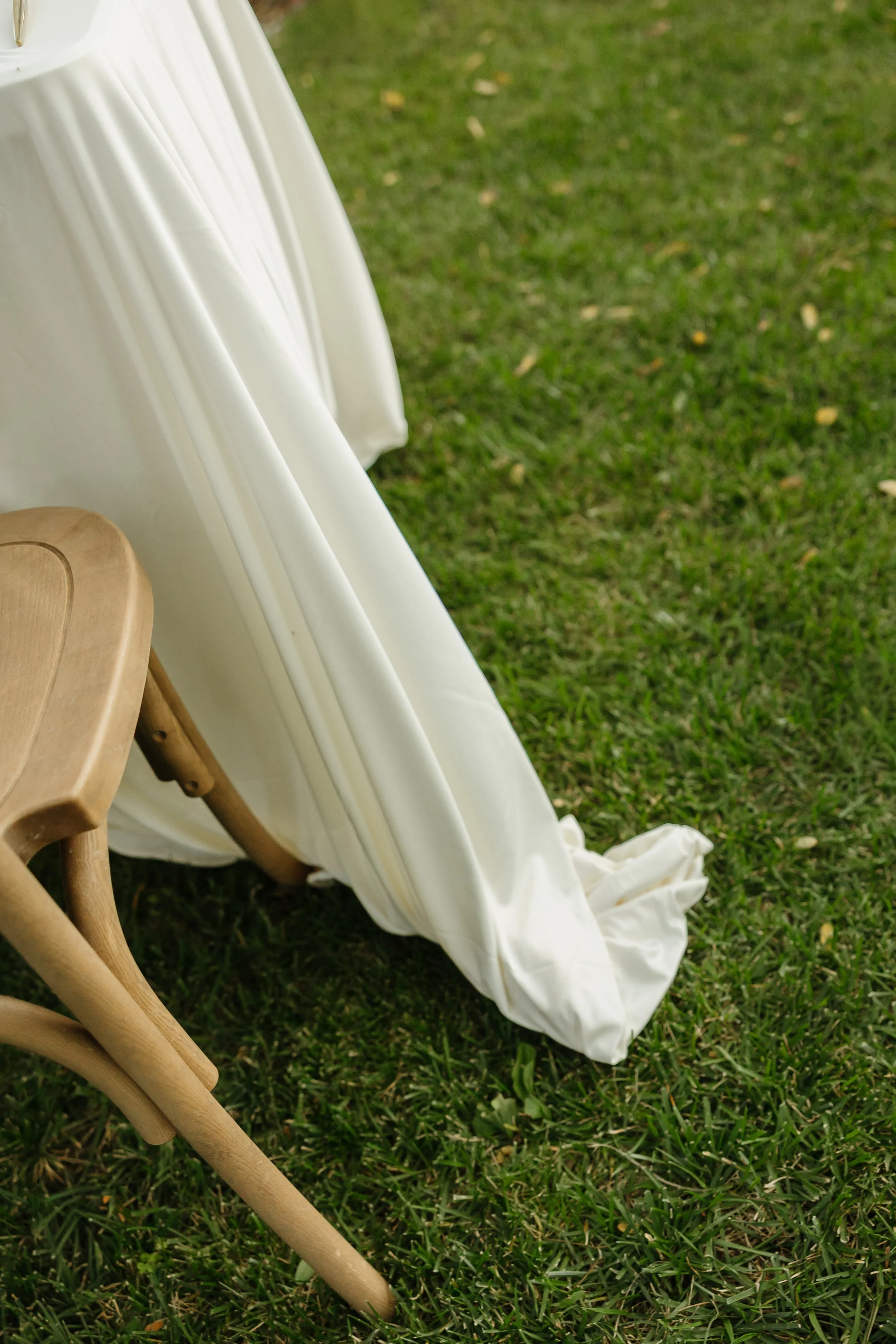 Close-up of a white, flowing fabric draped over a wooden chair on a grassy lawn.