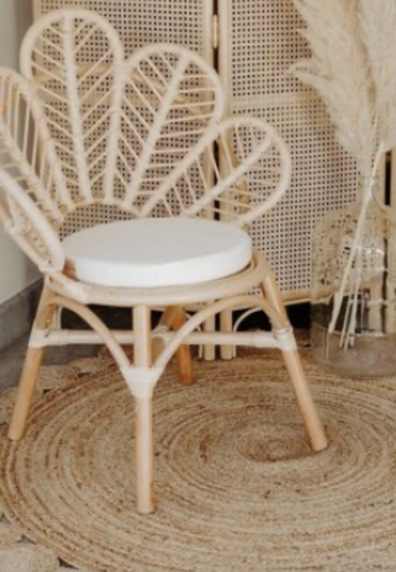 A wicker peacock chair with a white cushion placed on the seat, situated on a round woven rug.