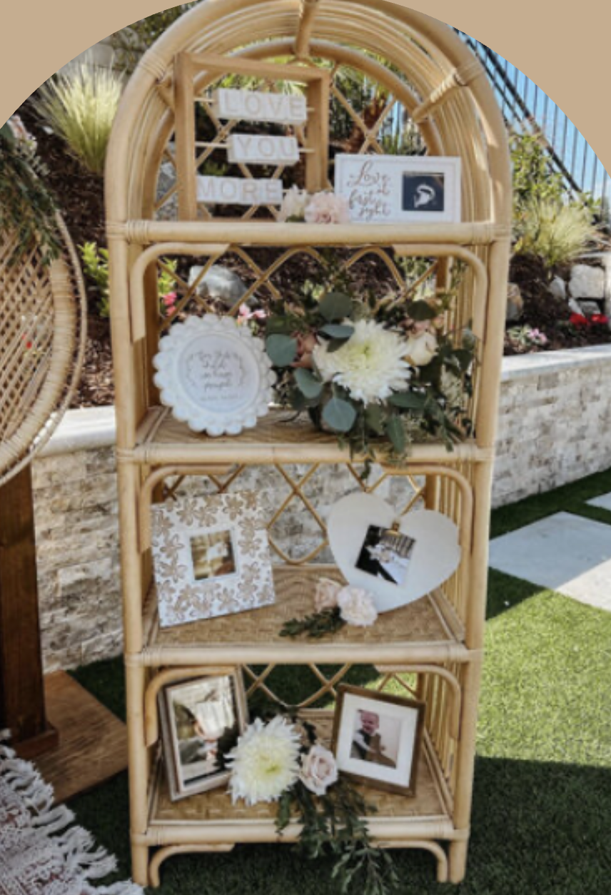Decorative wicker shelf with framed photos, flowers, and motivational signs outdoors.