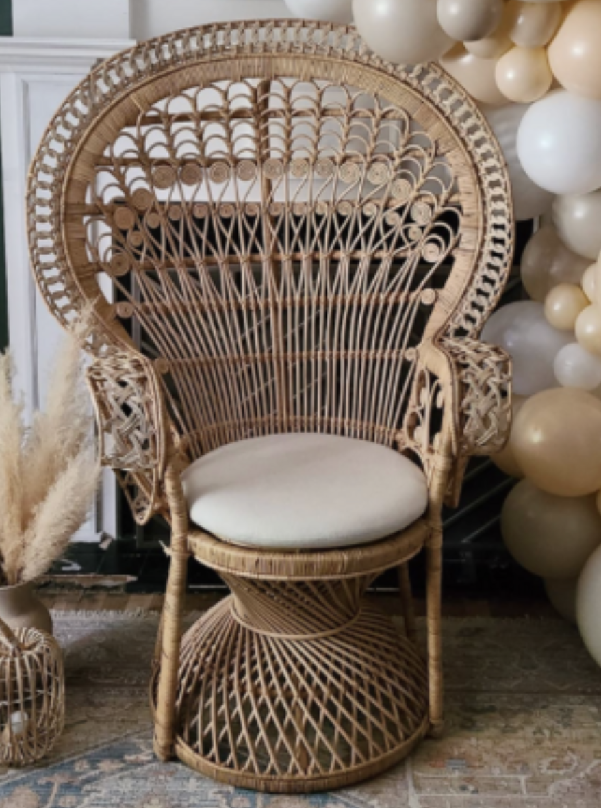 Decorative high-backed wicker chair with a cream cushion, surrounded by balloons in neutral colors, on a patterned floor.