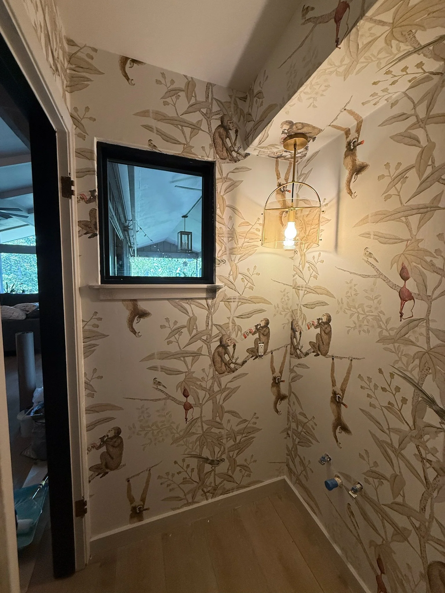 Small room with wallpaper featuring monkeys and leaves, a window, and a hanging light fixture.