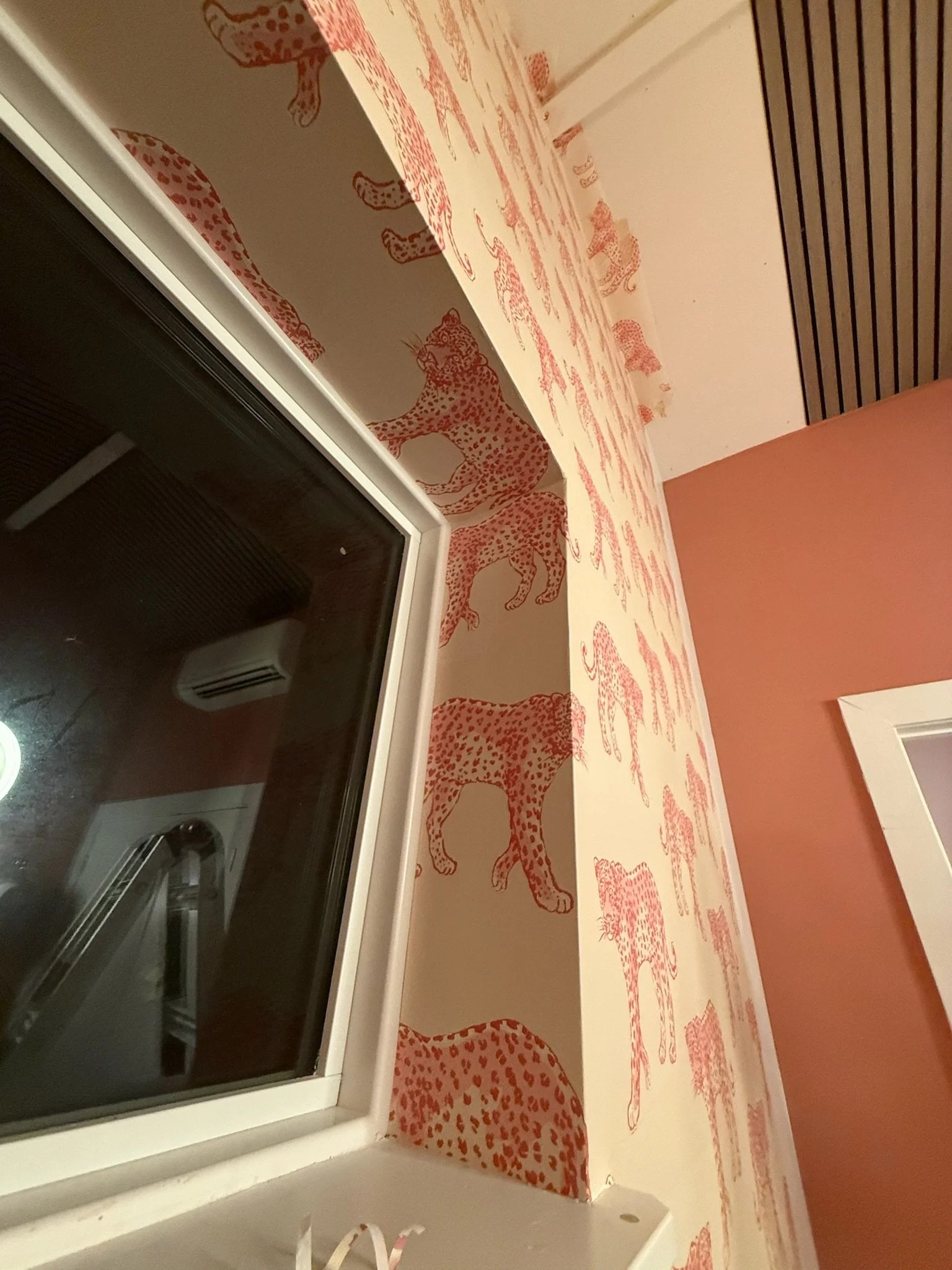 A wall with wallpaper featuring orange leopard illustrations in a repeating pattern.