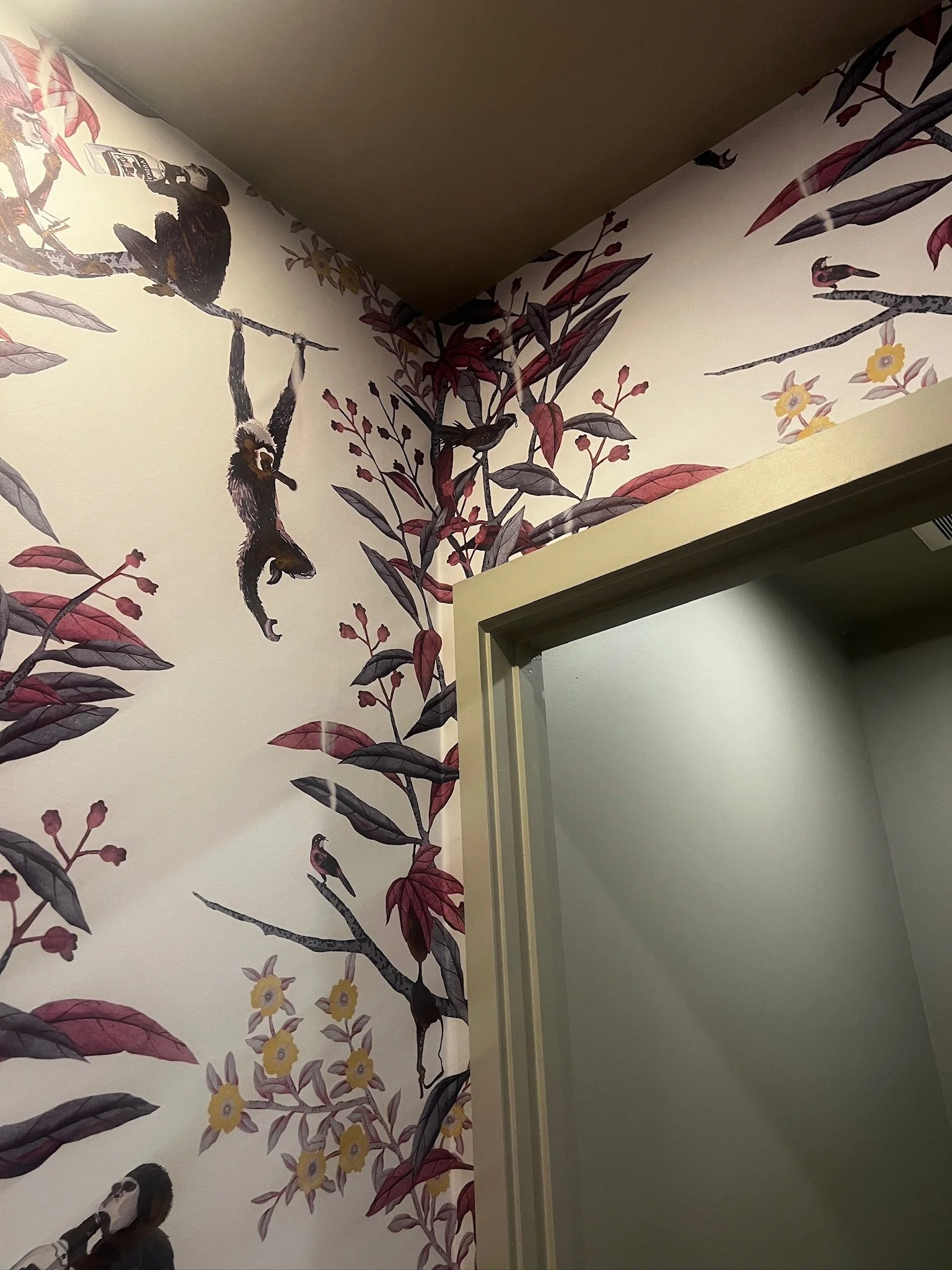 Interior wall with a mural depicting various birds and leaves, including a monkey hanging from a branch and perched birds among foliage.