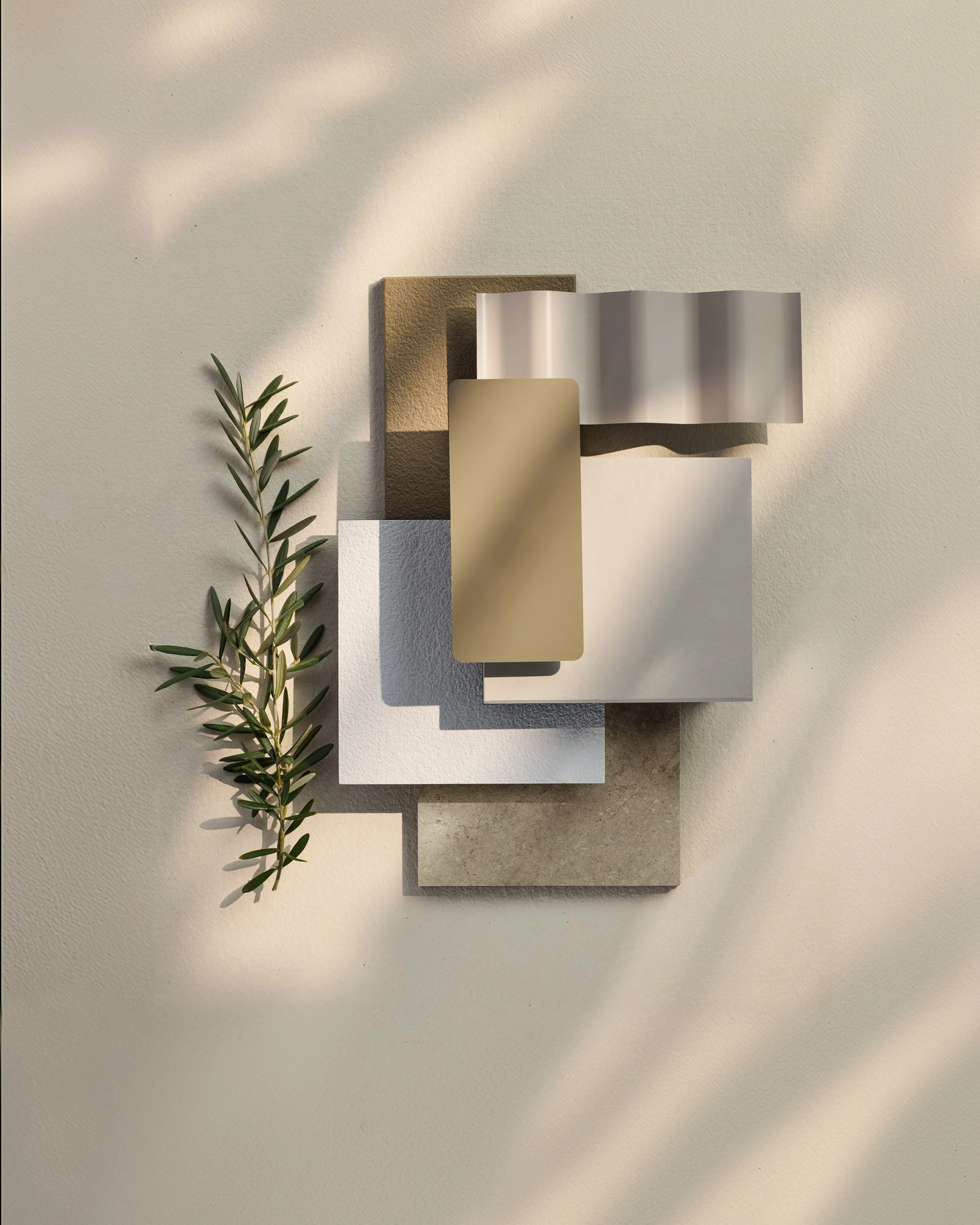 Arrangement of various textured and colored paper or fabric swatches with a sprig of greenery on a beige surface.