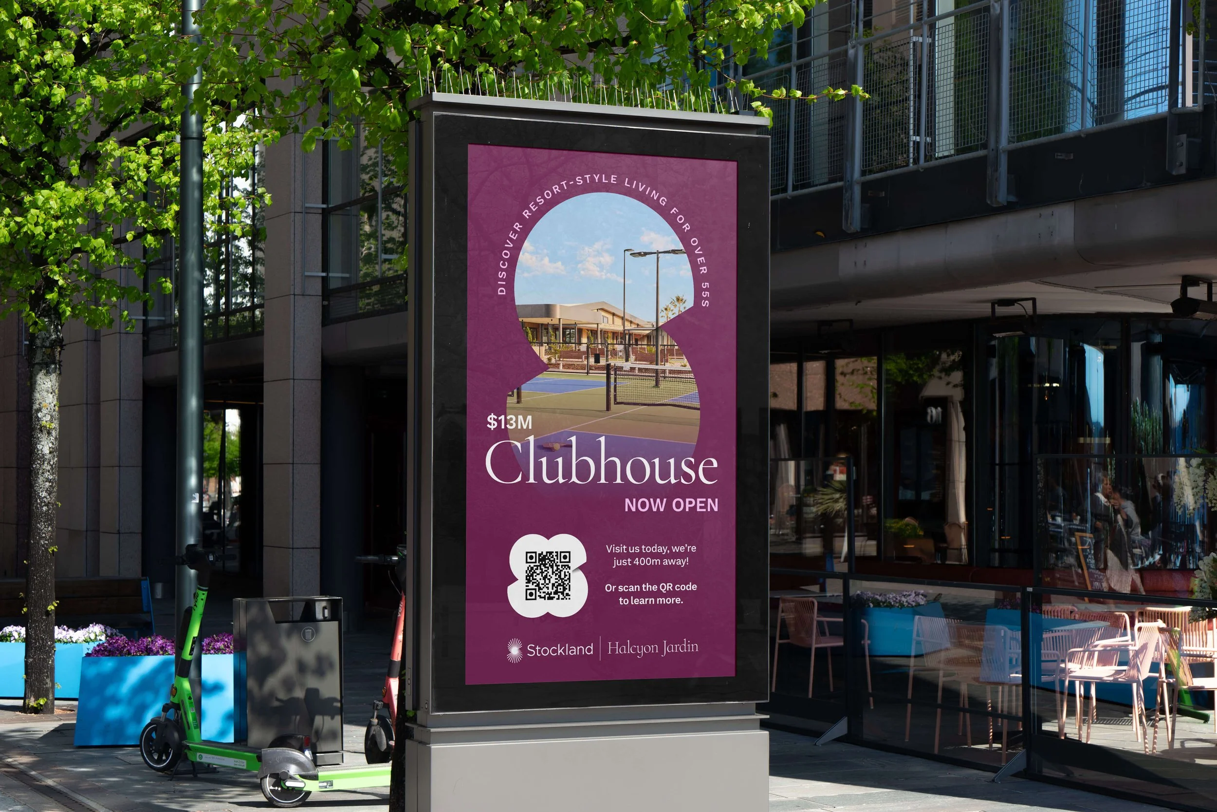 Digital billboard advertising a new clubhouse opening at Stockland Halcyon Jardin, with a picture of a tennis court and modern residential buildings, featuring a purple background and white text.