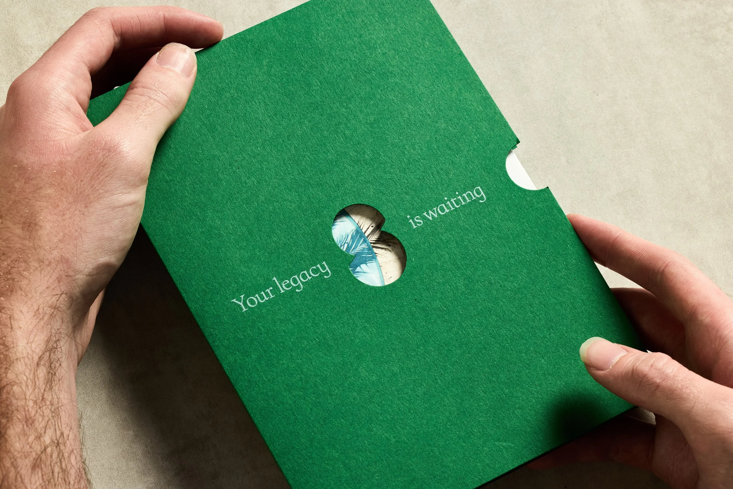 A person holding a green card with a circular cutout revealing a message inside. The message reads, 'Your legacy is waiting'.