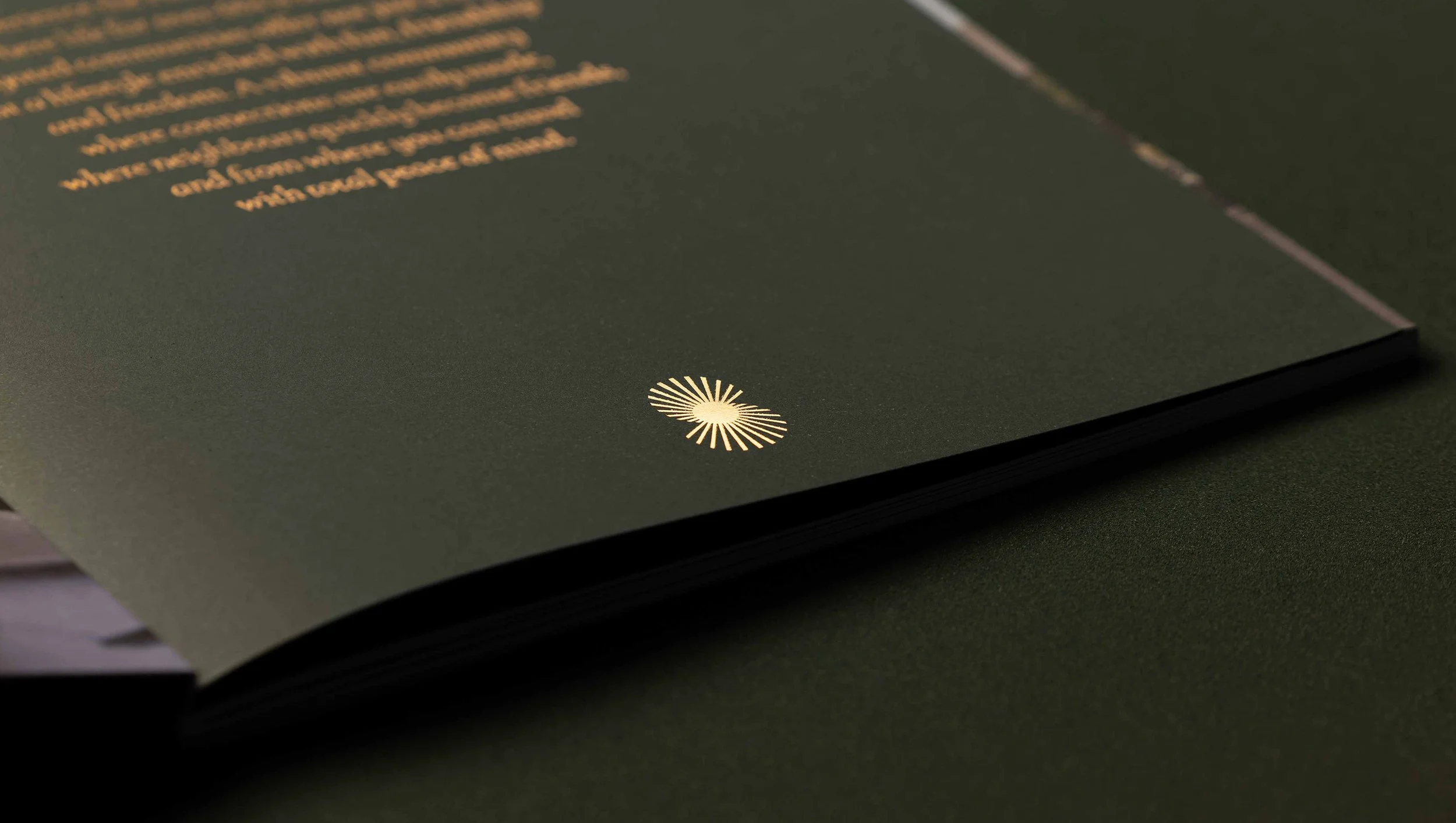 A close-up of a page from a dark-colored booklet or brochure, with a glowing gold or yellow circular emblem featuring radiating lines at the bottom center, and text in a similar color on the upper part of the page.