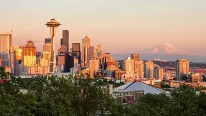 Seattle skyline at sunset with the Space Needle in the foreground and Mount Rainier in the background.