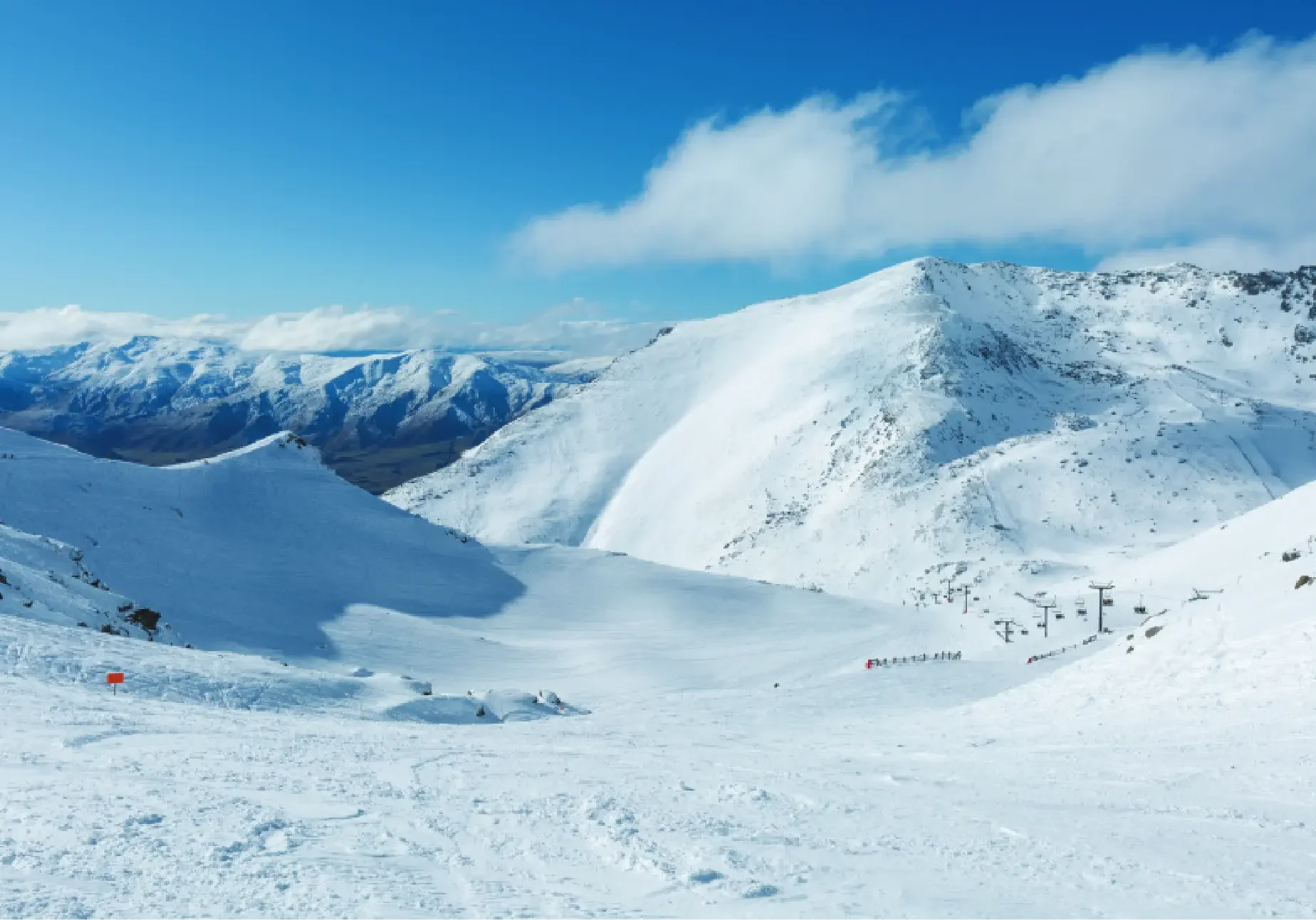 Snow-covered mountain landscape with ski lifts and a clear blue sky.