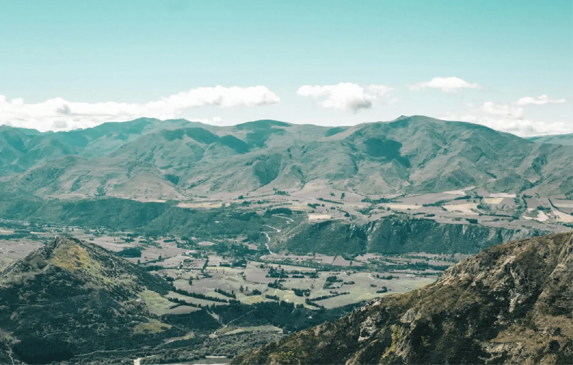 Scenic view of green mountains and a valley with farmland under a partly cloudy sky.