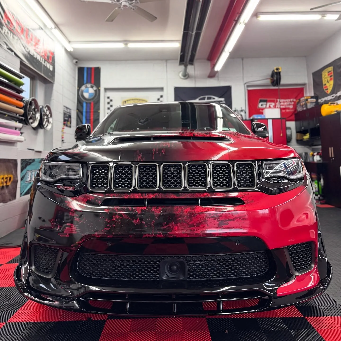 Front view of a red and black sports car in a garage with car accessories and banners.