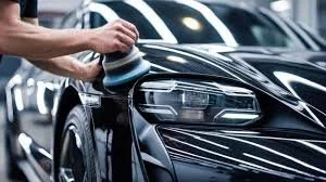 Person polishing or cleaning a black car with a cloth in a parking lot.