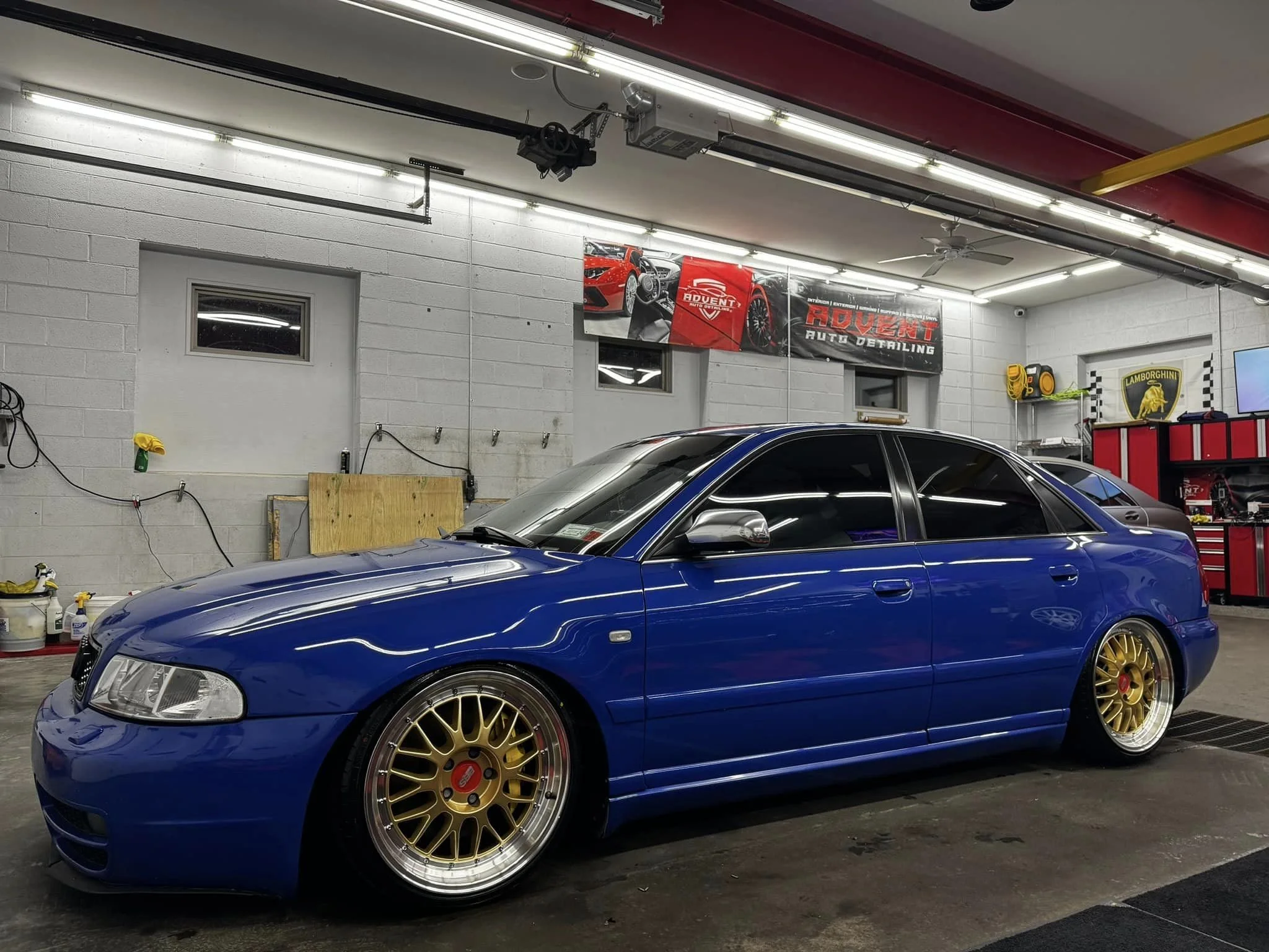 A blue car with gold wheels parked inside an auto detailing garage.