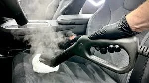 Person using a handheld steam cleaner to clean the car interior, producing steam.