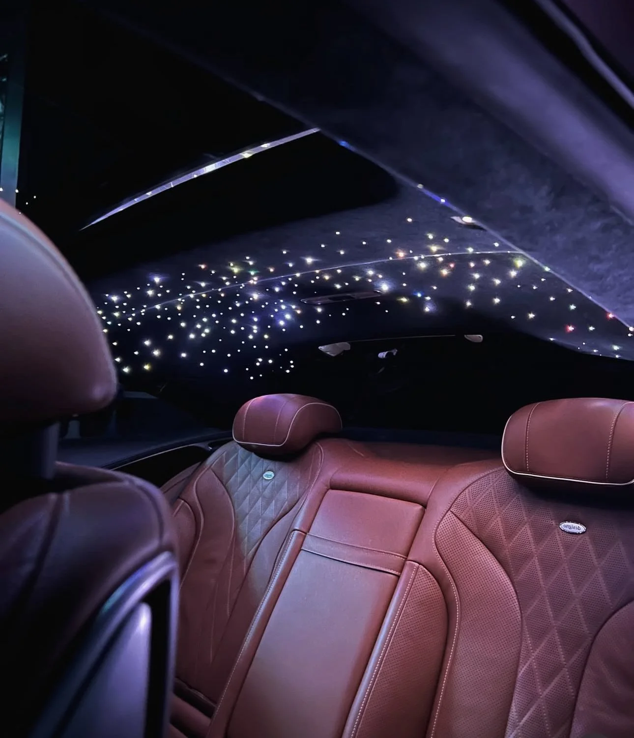 The interior of a luxury car with brown leather seats and a starry LED ceiling display.