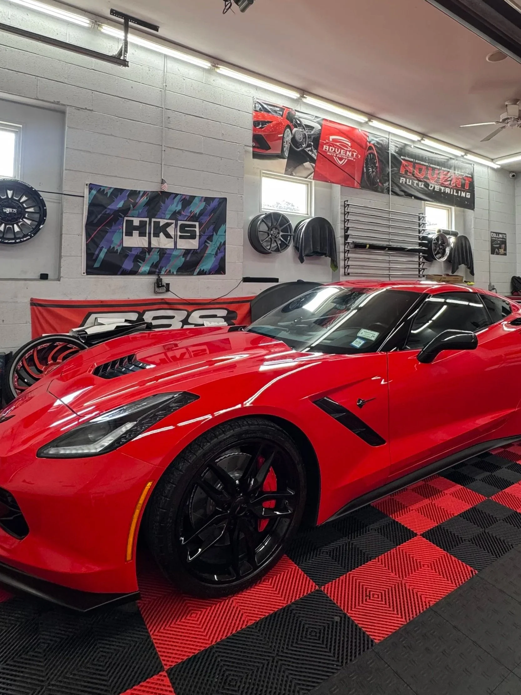 Red sports car inside a garage with racing banners and wheels on the wall.