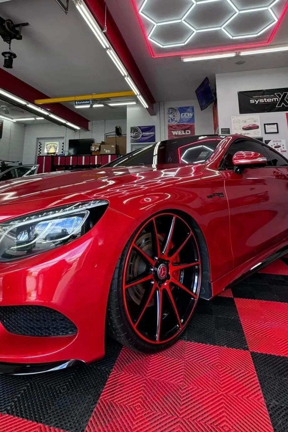 Red sports car with black and red wheels inside an automotive workshop.