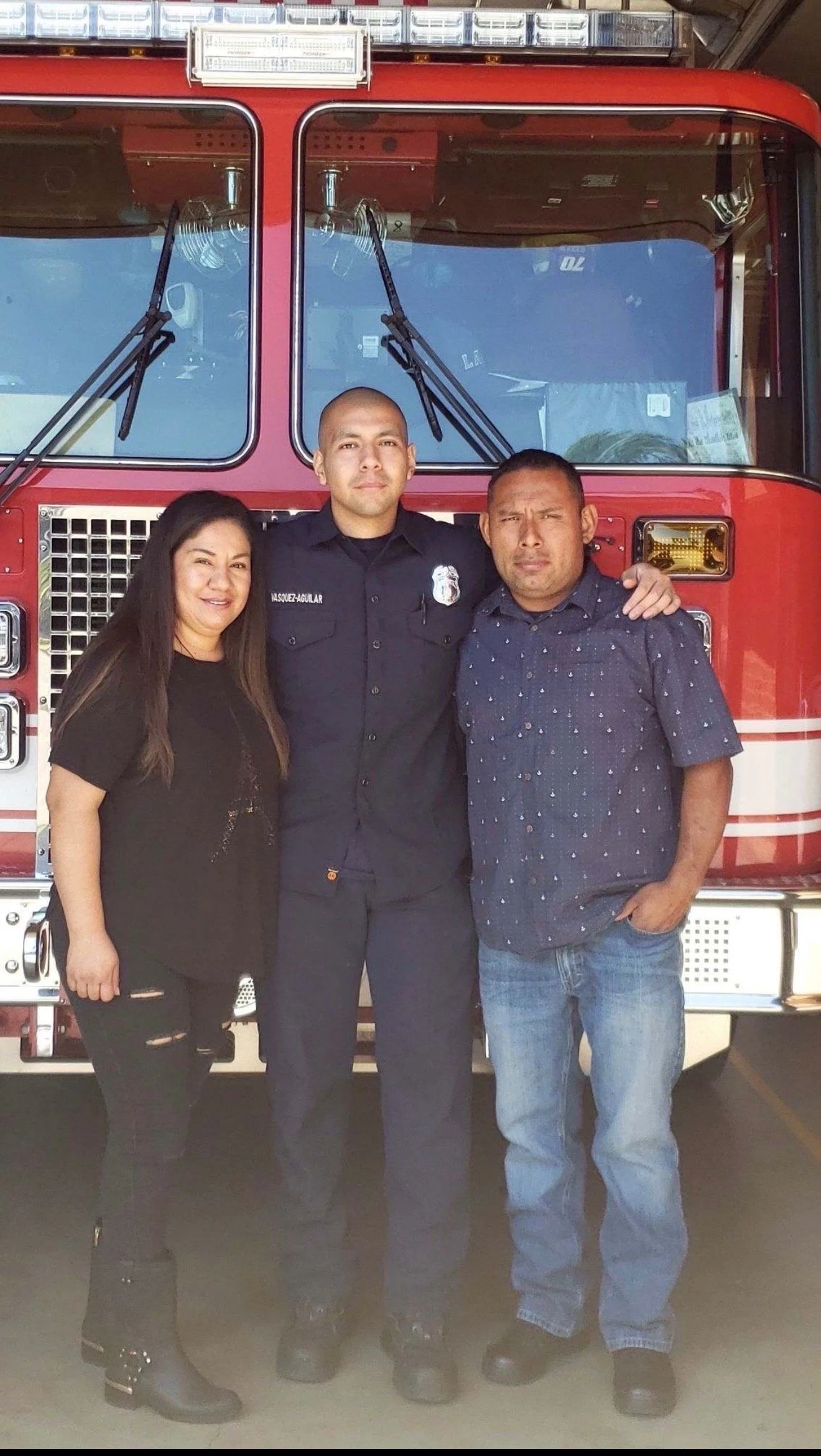 Three people standing in front of a red fire truck, smiling at the camera.
