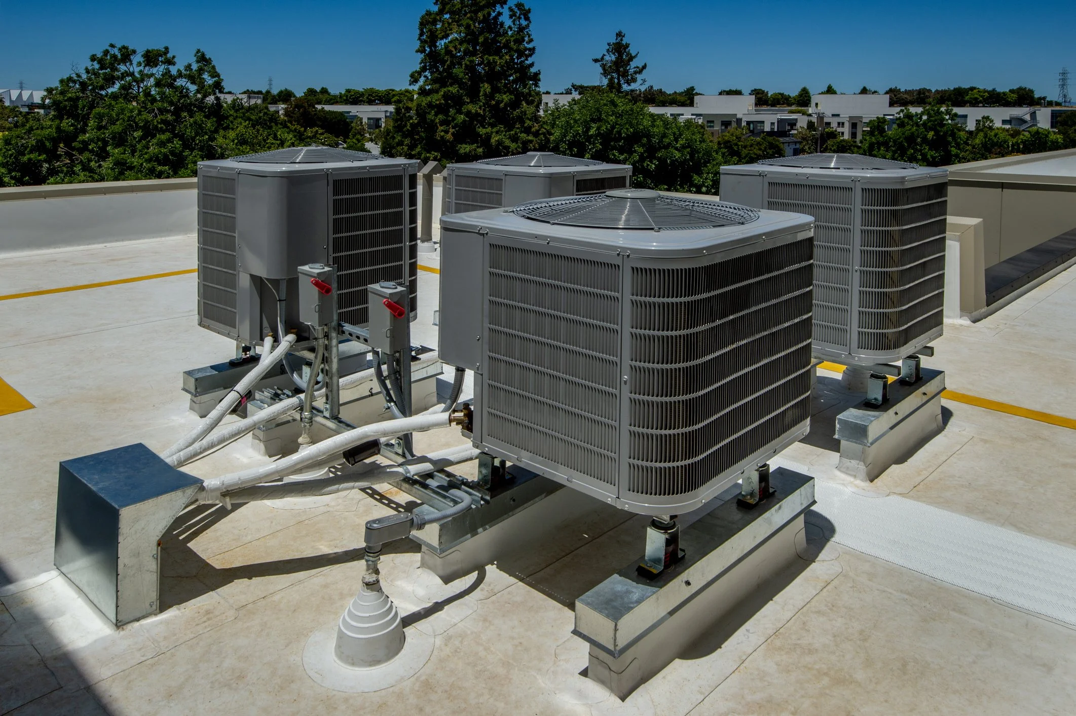 Multiple large HVAC units installed on a flat rooftop with trees and buildings in the background.