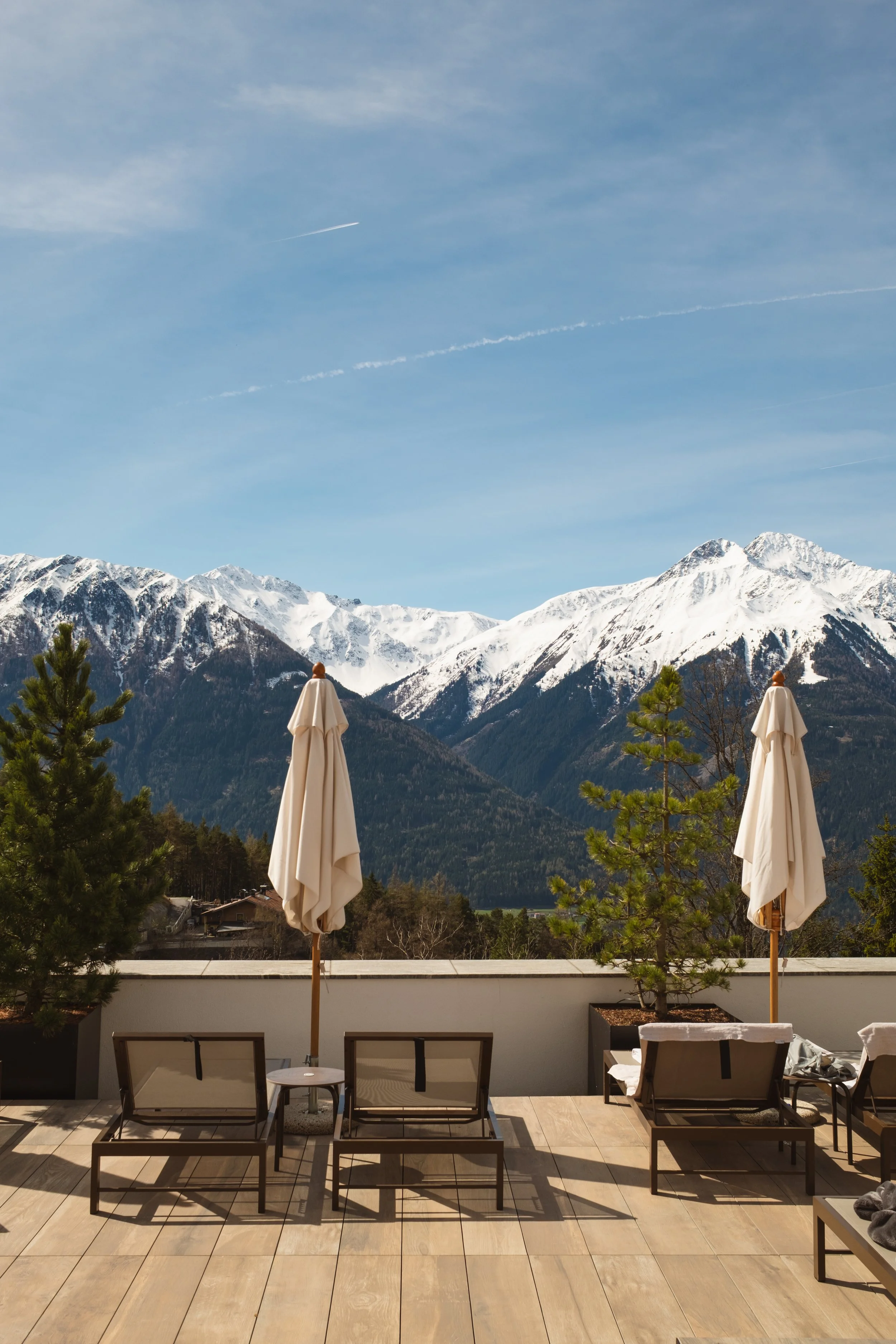 View of a mountain range with snow-capped peaks, taken from a terrace with chairs and umbrellas, under a clear blue sky.