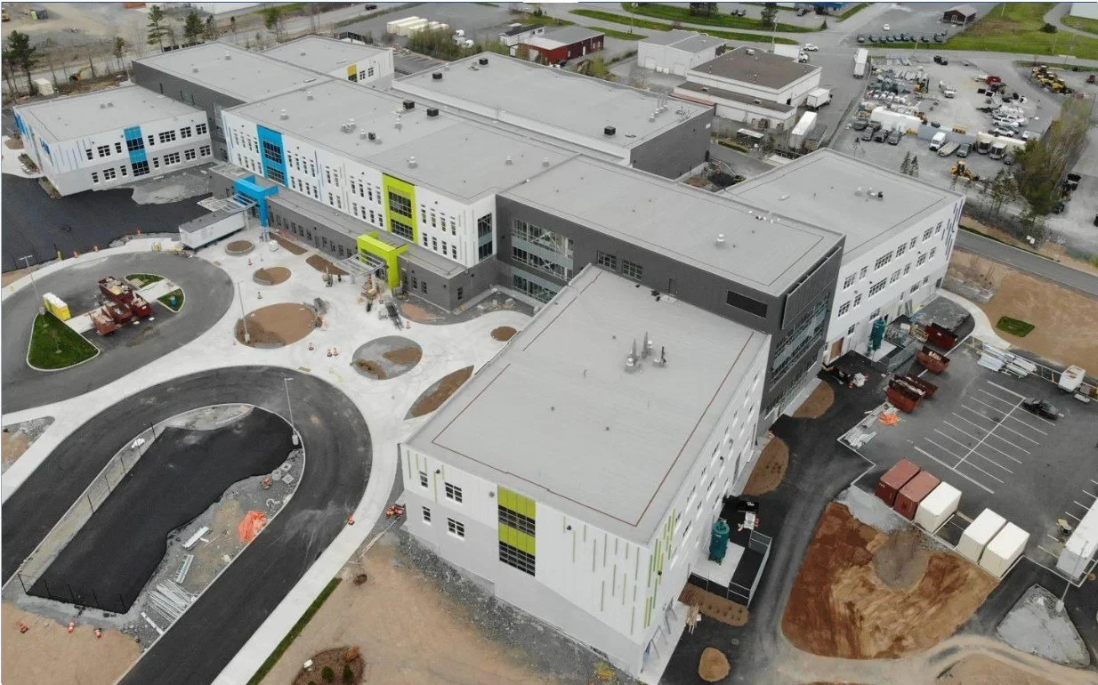 Aerial view of a modern school building under construction with landscaped areas, parking lot, and surrounding urban infrastructure.