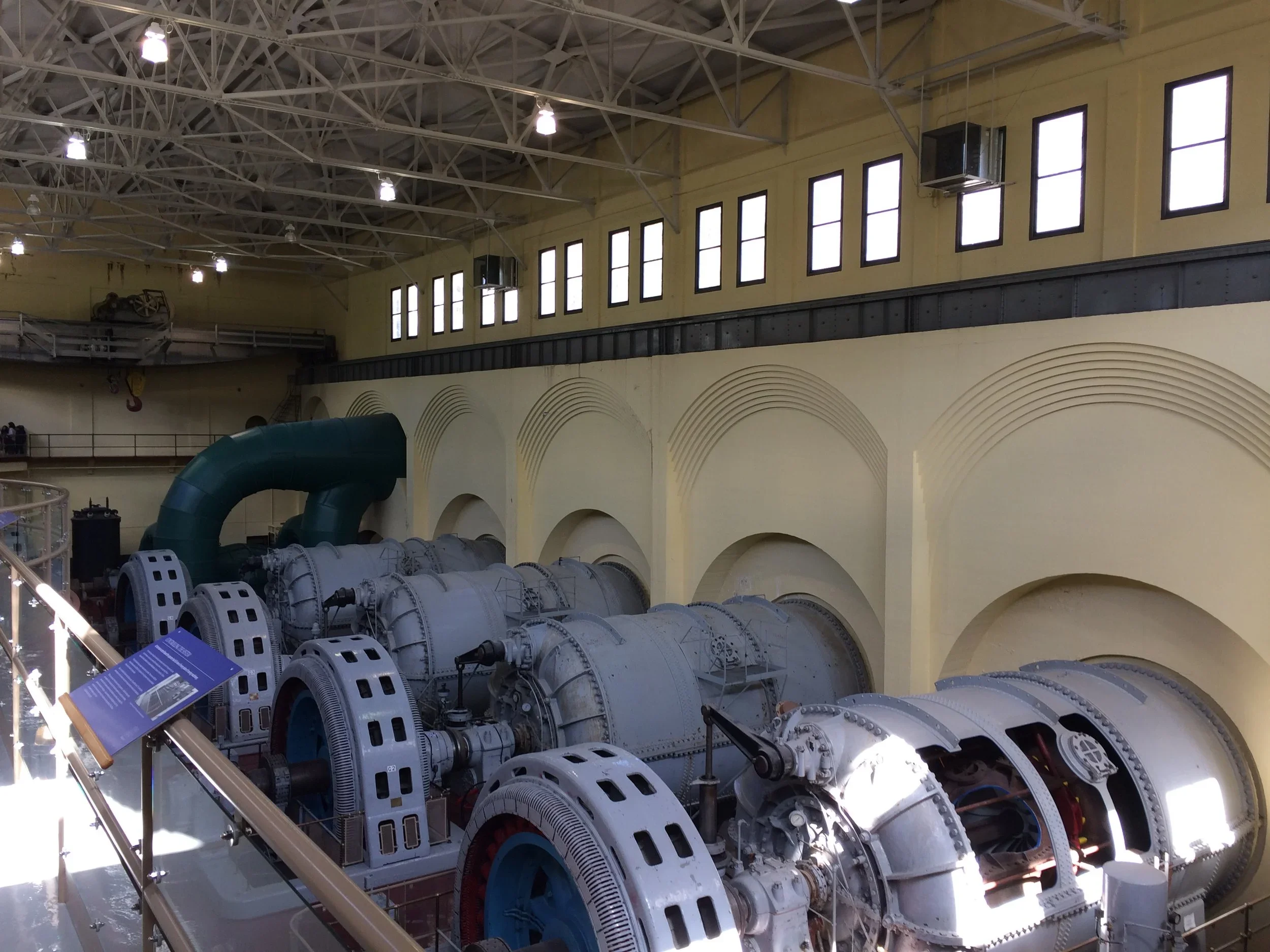 Large industrial turbines inside a spacious museum or industrial facility with high ceilings and numerous windows.