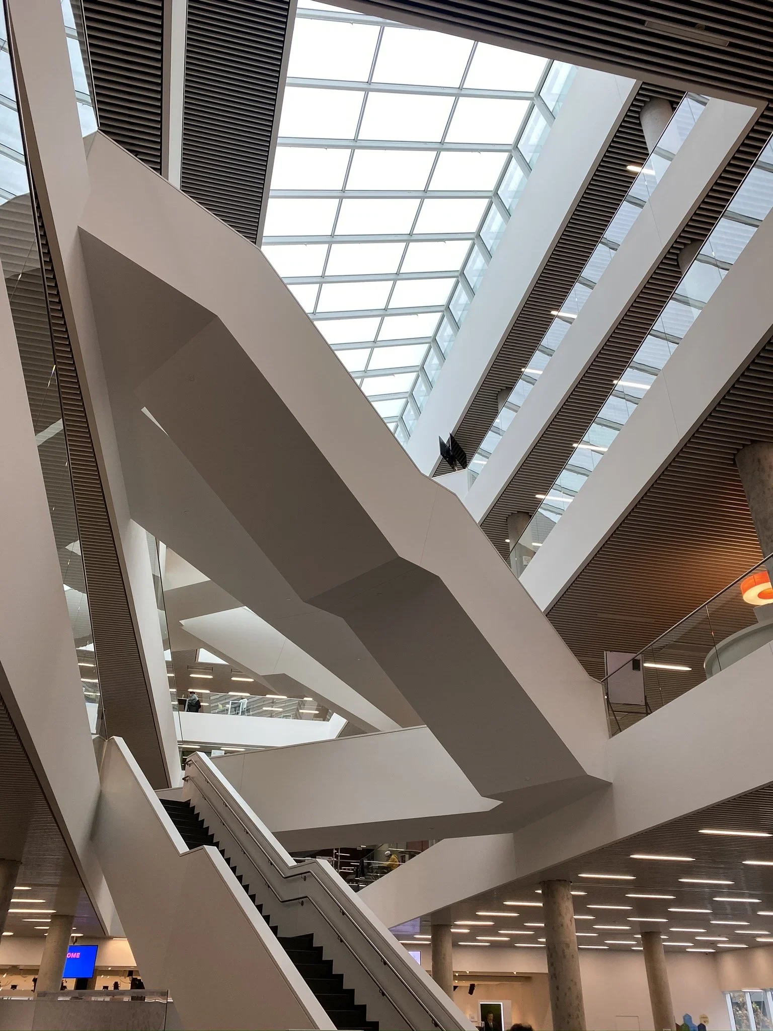 Interior view of a modern multi-story building with escalators and a large glass ceiling.