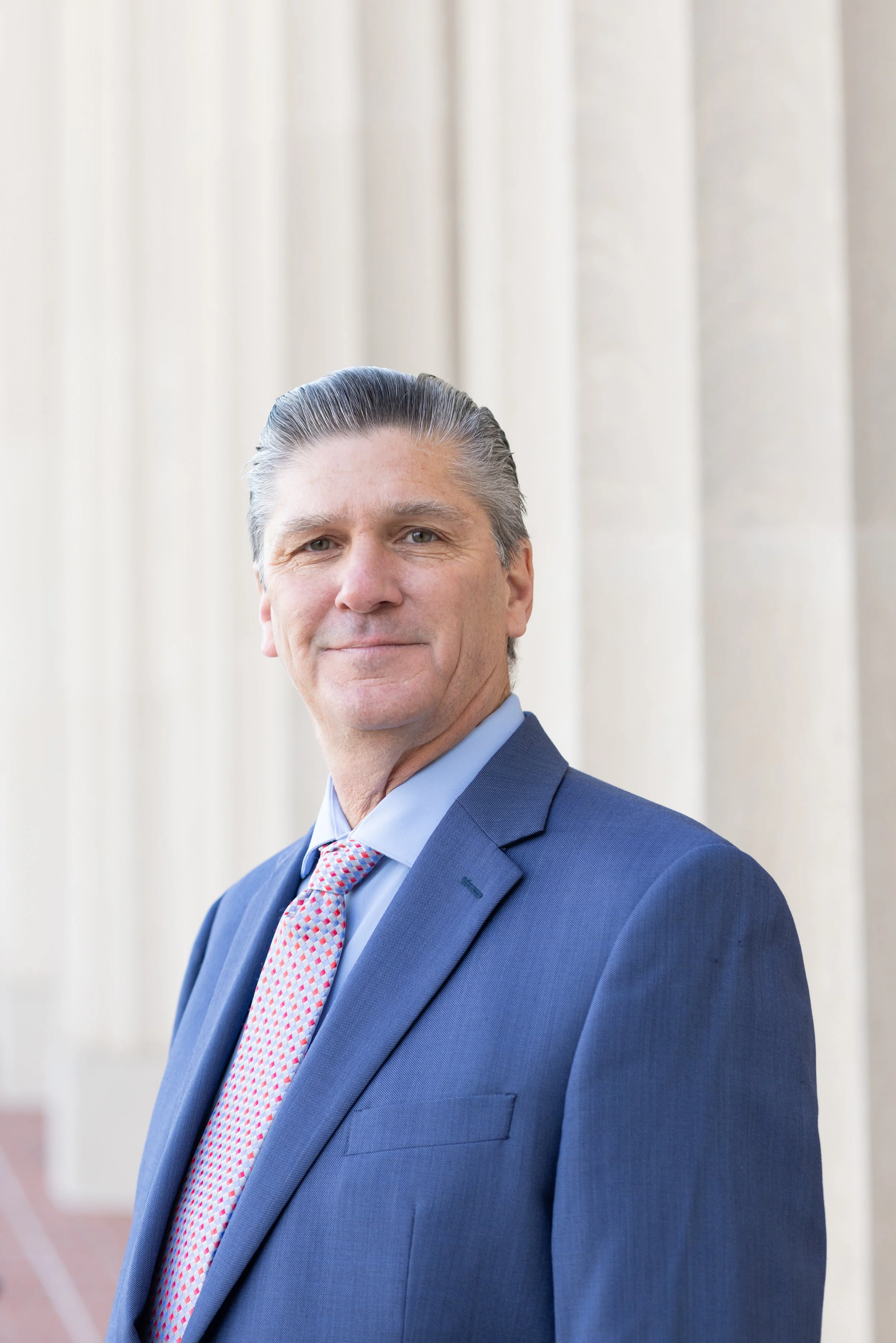 Northern California Eminent Domain Attorney in a blue suit, white shirt, and striped tie, standing in front of courthouse columns prepared to defend property owners' rights against condemnation lawsuits in California