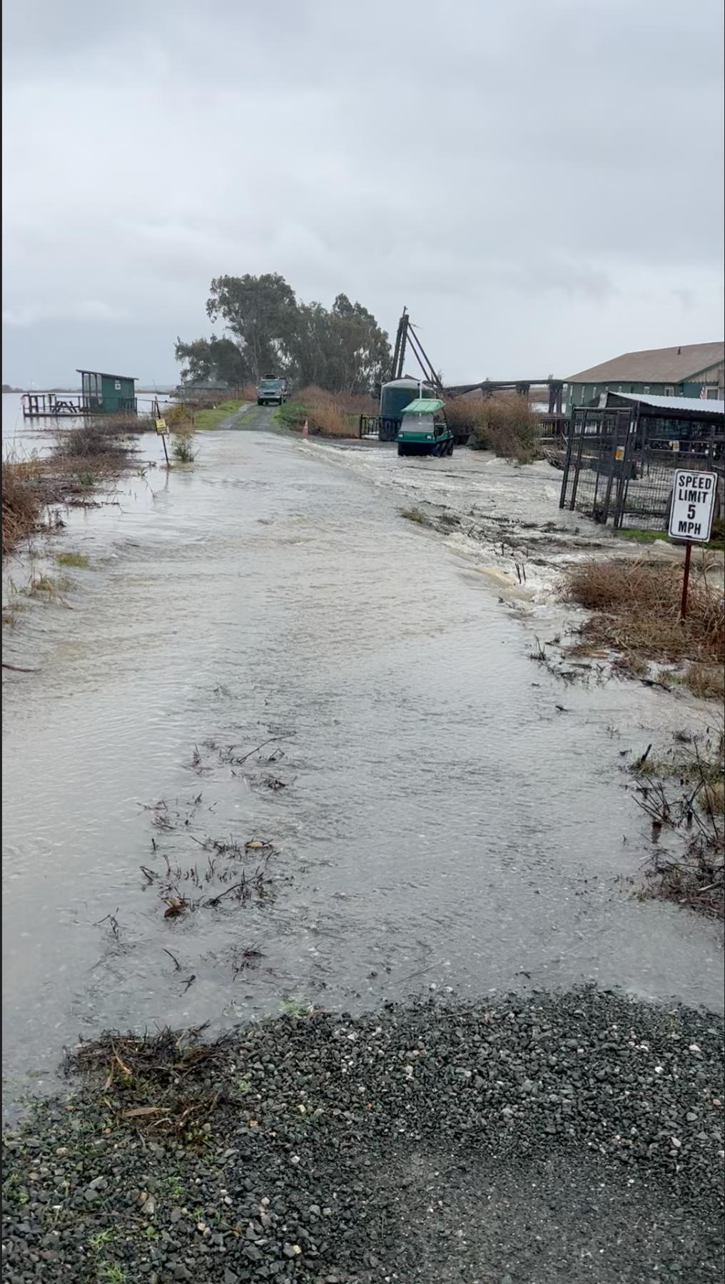 Flooded road with water covering the street and surrounding areas, and some damaged structures and vehicles in a cloudy, overcast environment,  highlighting Jenny & Jenny's inverse condemnation experience in Northern California.