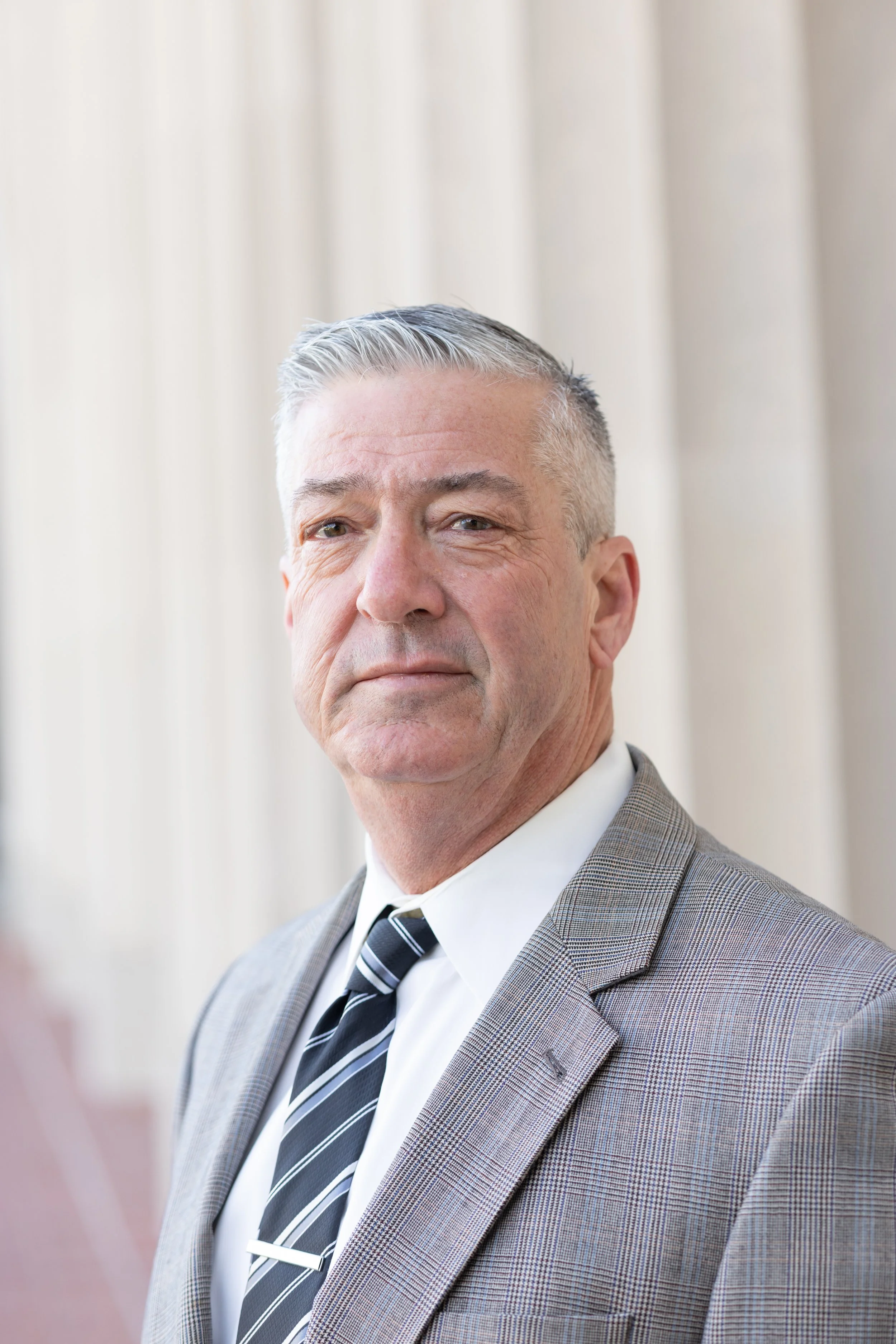 Northern California Eminent Domain Attorney in a gray checked suit, white shirt, and striped tie, standing in front of courthouse columns prepared to defend property owners' rights against condemnation lawsuits in California