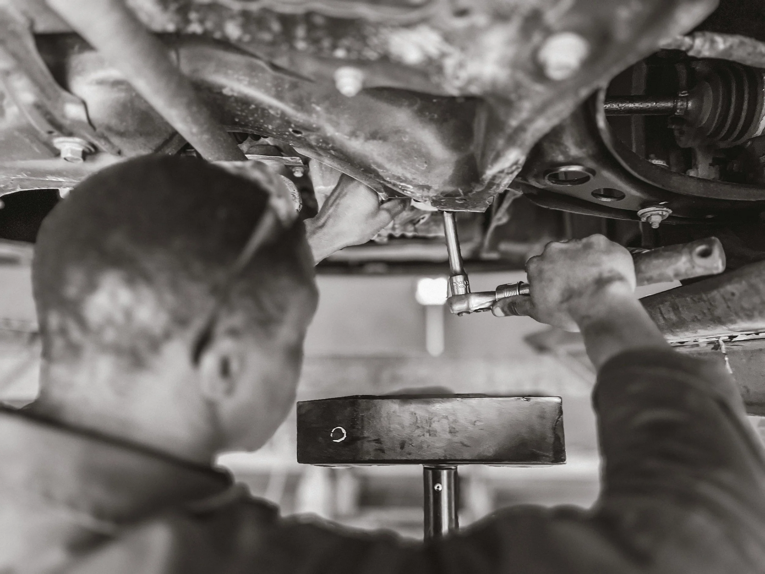 Vehicle undergoing WOF inspection in automotive workshop Mechanic inspecting car suspension for WOF compliance Car brake inspection during WOF check Vehicle safety inspection before WOF certification