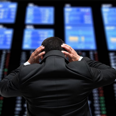 A person in a suit looking at multiple flight information screens at an airport or transportation hub, holding their head with both hands.