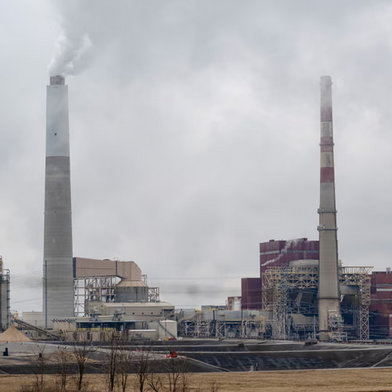Industrial power plant with two tall smokestacks emitting smoke on a cloudy day