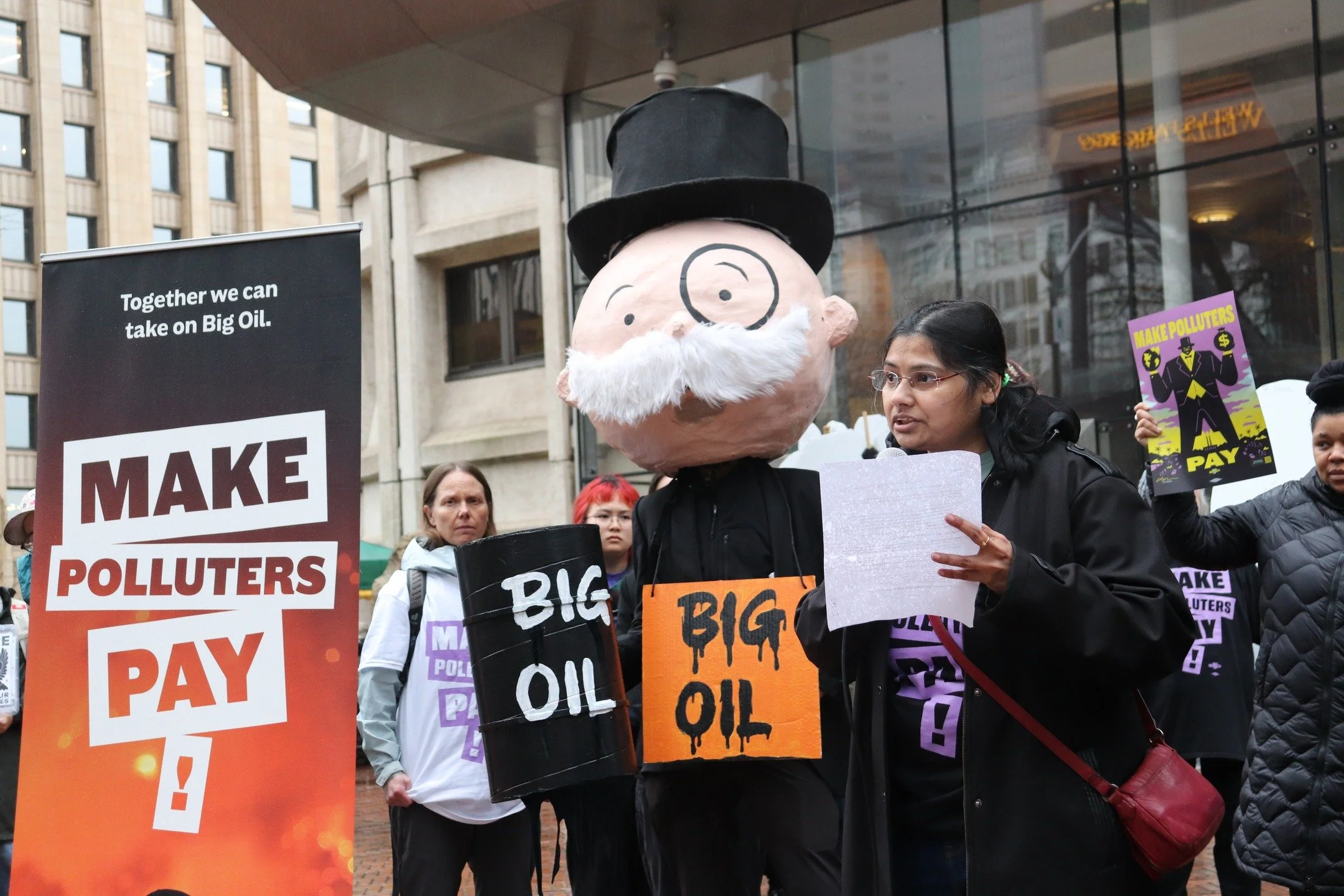 Protesters holding signs about pollution and Big Oil in an urban setting.