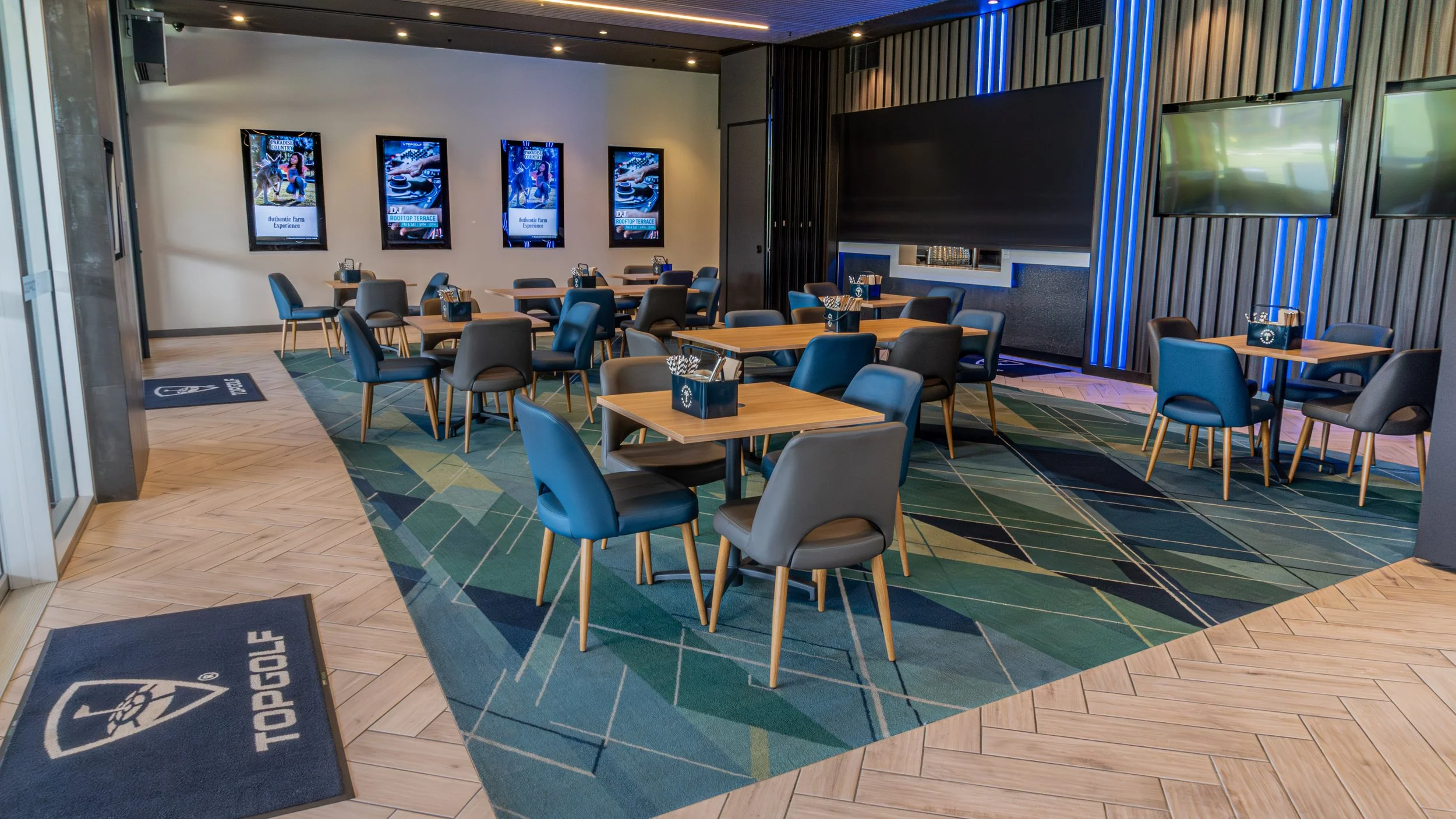 An empty indoor dining or lounge area with tables, chairs, and wall-mounted screens in a modern setting.