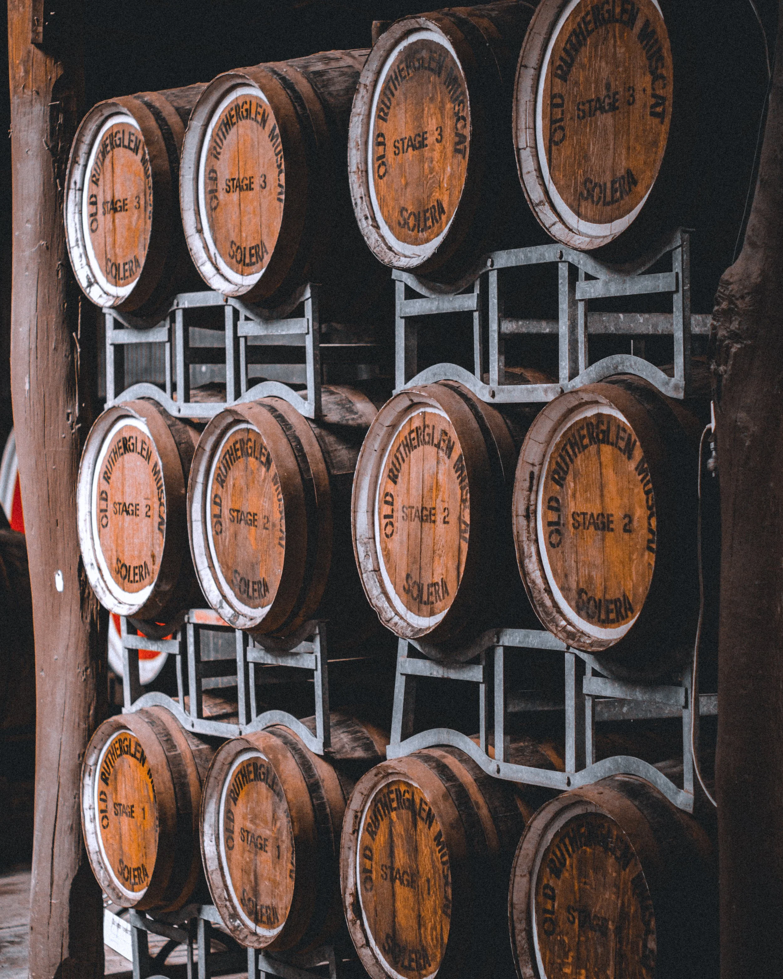Stacked barrels labeled with stages, in a winery, on metal racks.