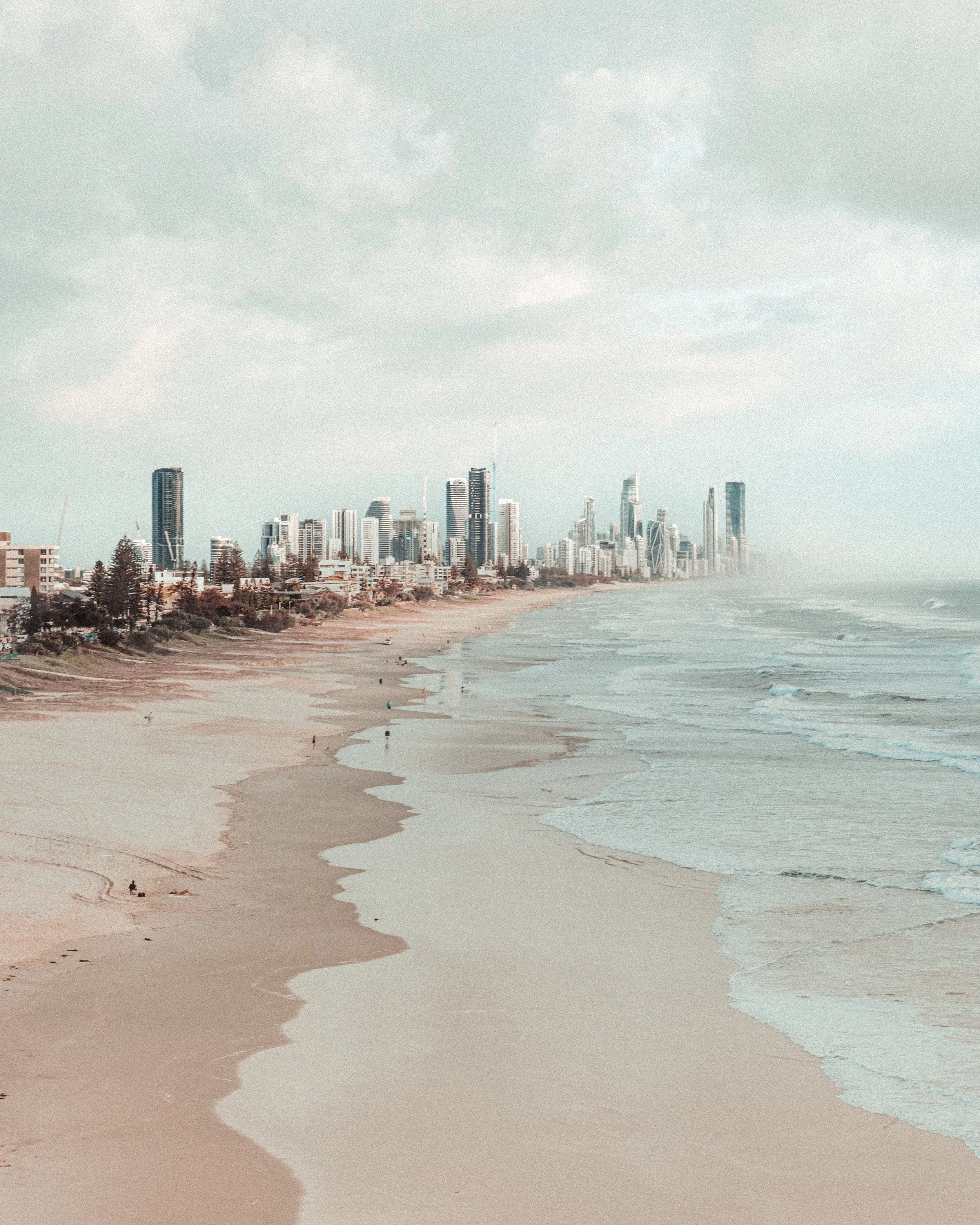 Beach with Gold Coast city skyline in the background and a cloudy sky.