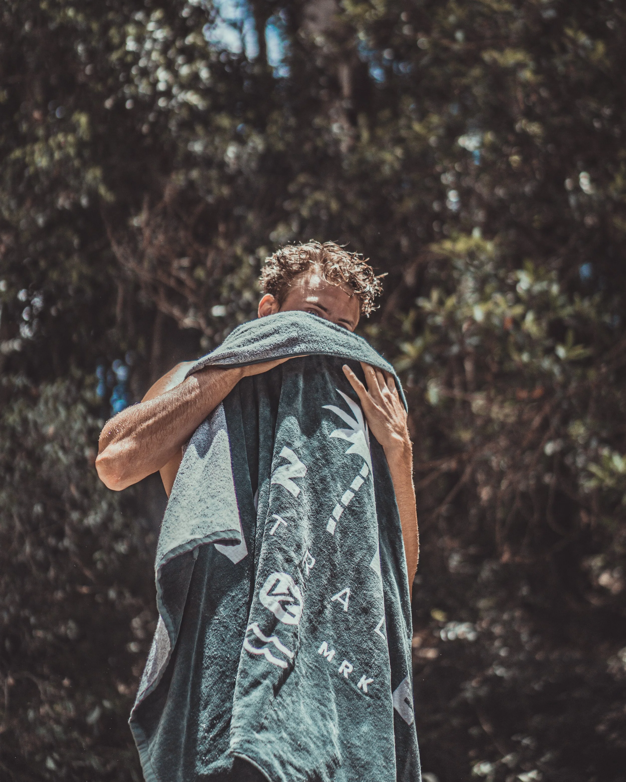A person hugging a towel with designs on it, outdoors, with trees in the background.