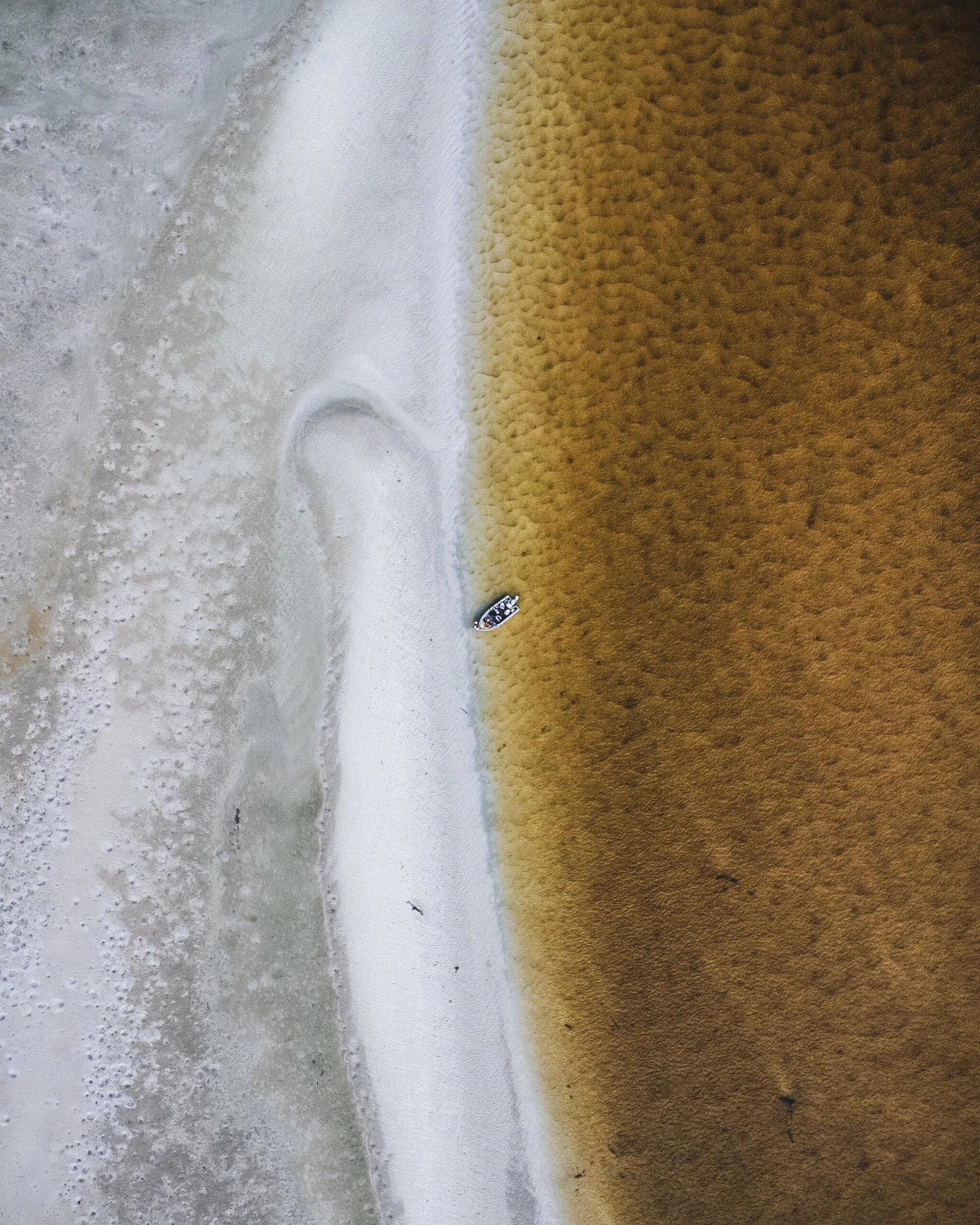 Aerial view of a boat on Whitehaven beach where sand meets water with brown water and white foam.