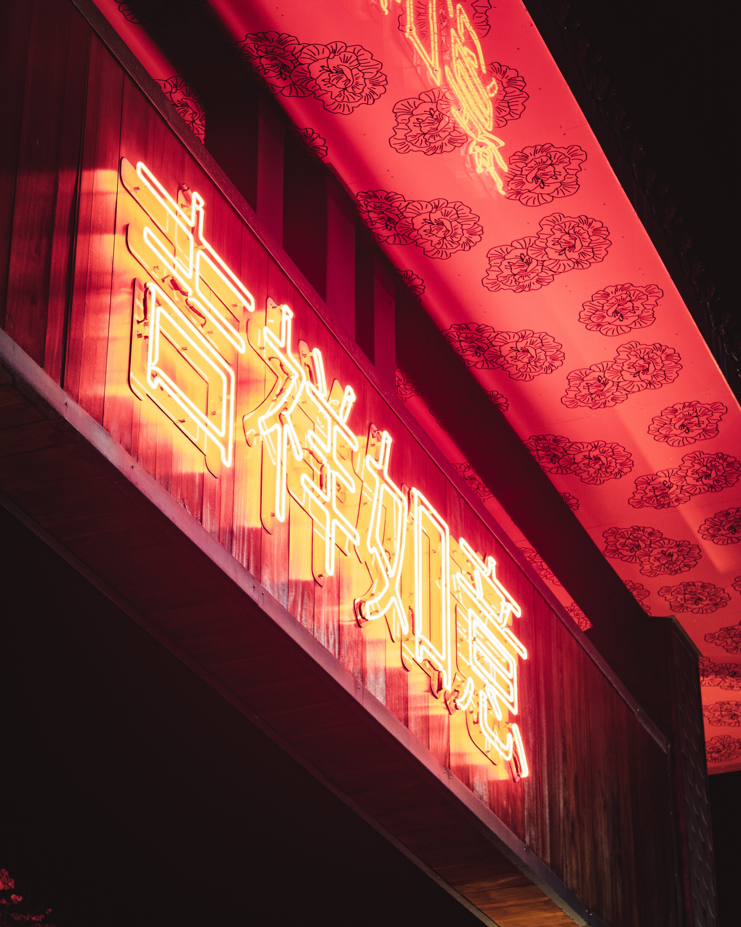 Neon sign with Chinese characters on a red wooden background, under a ceiling with red floral patterns.