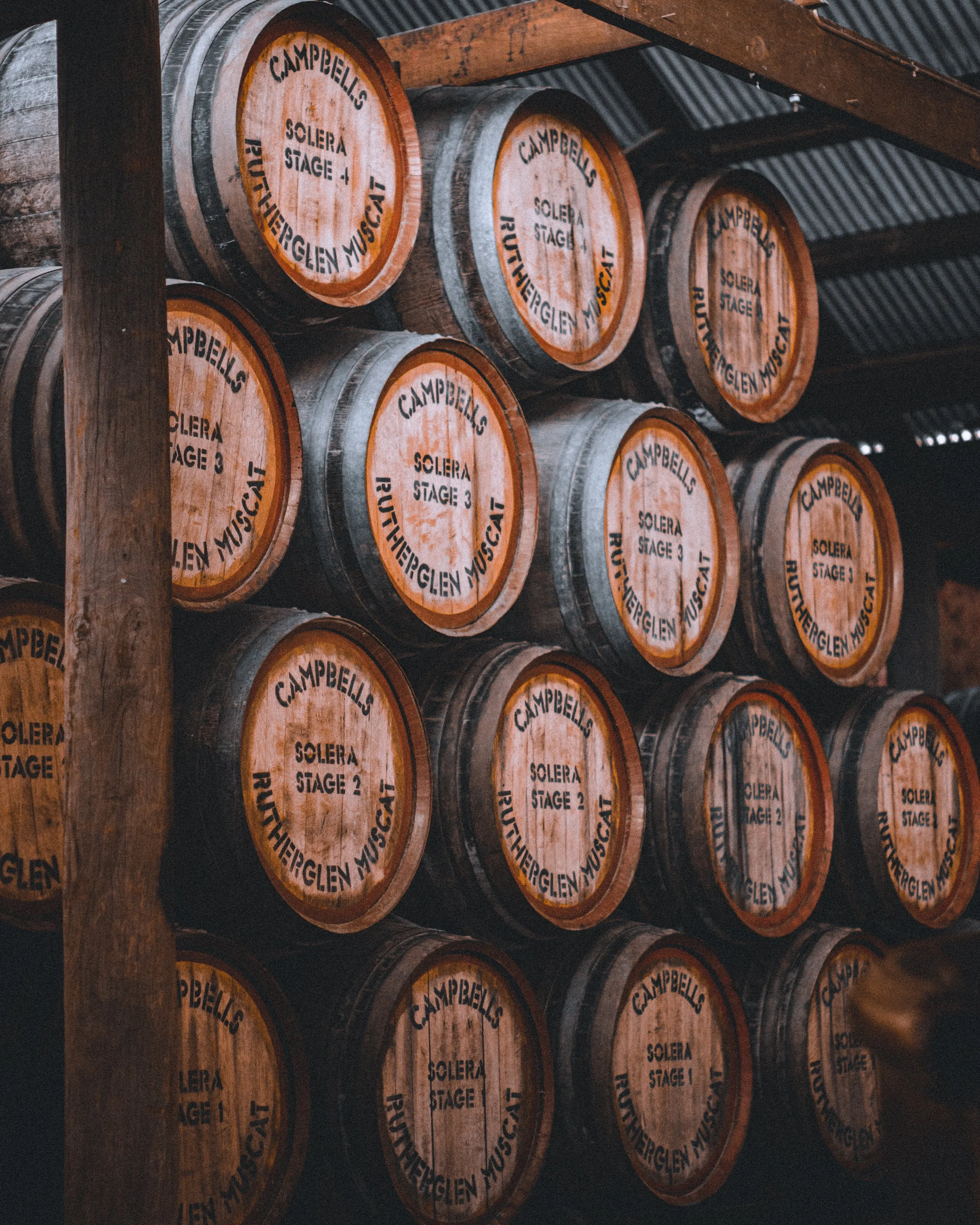 Multiple wooden barrels stored on a rack, labeled with 'Campbell's,' 'Solera Stage,' and numbered stages, inside a cellar or storage area.