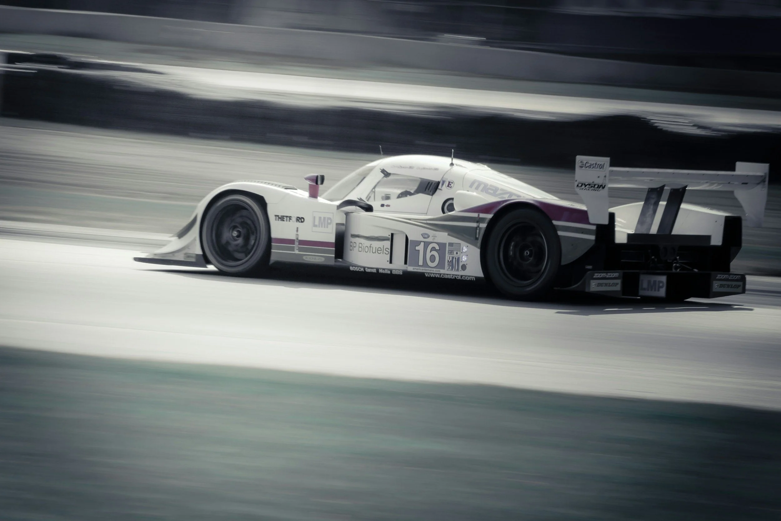 A white and purple race car speeding on a track with motion blur in the background.