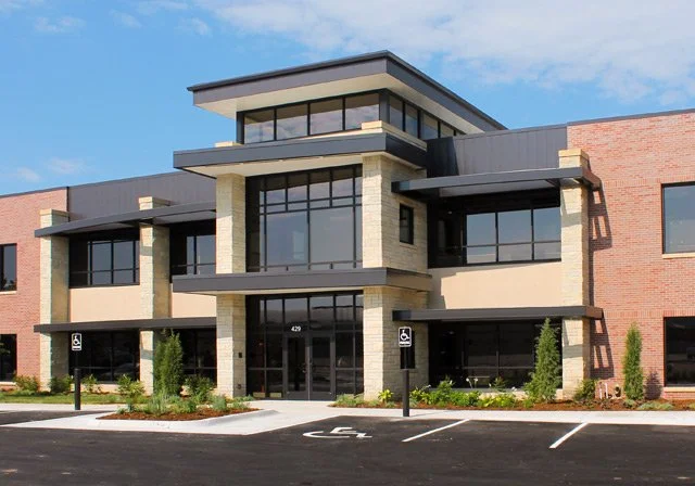 Modern two-story commercial building with large glass windows, brick and beige walls, and handicapped parking spaces in front.