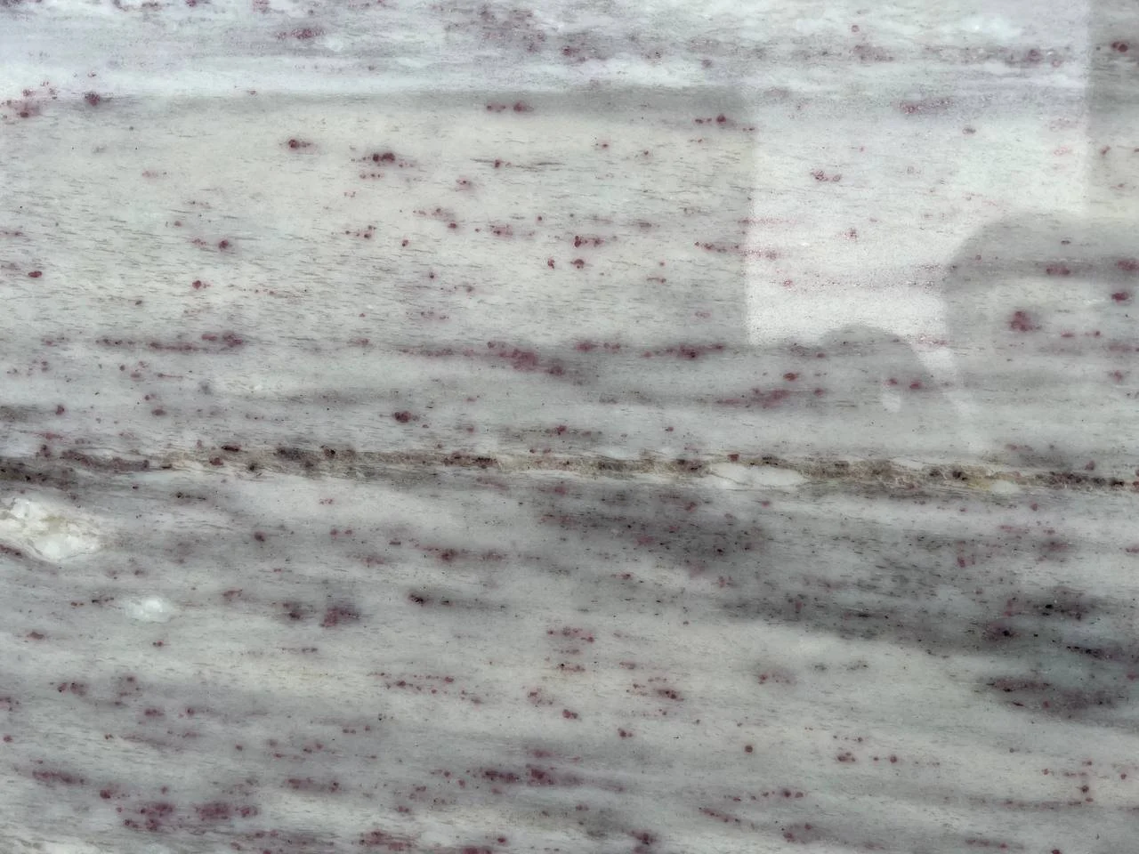 New River White Granite. A Close-up of a marble surface with white, gray, and dark red speckles.